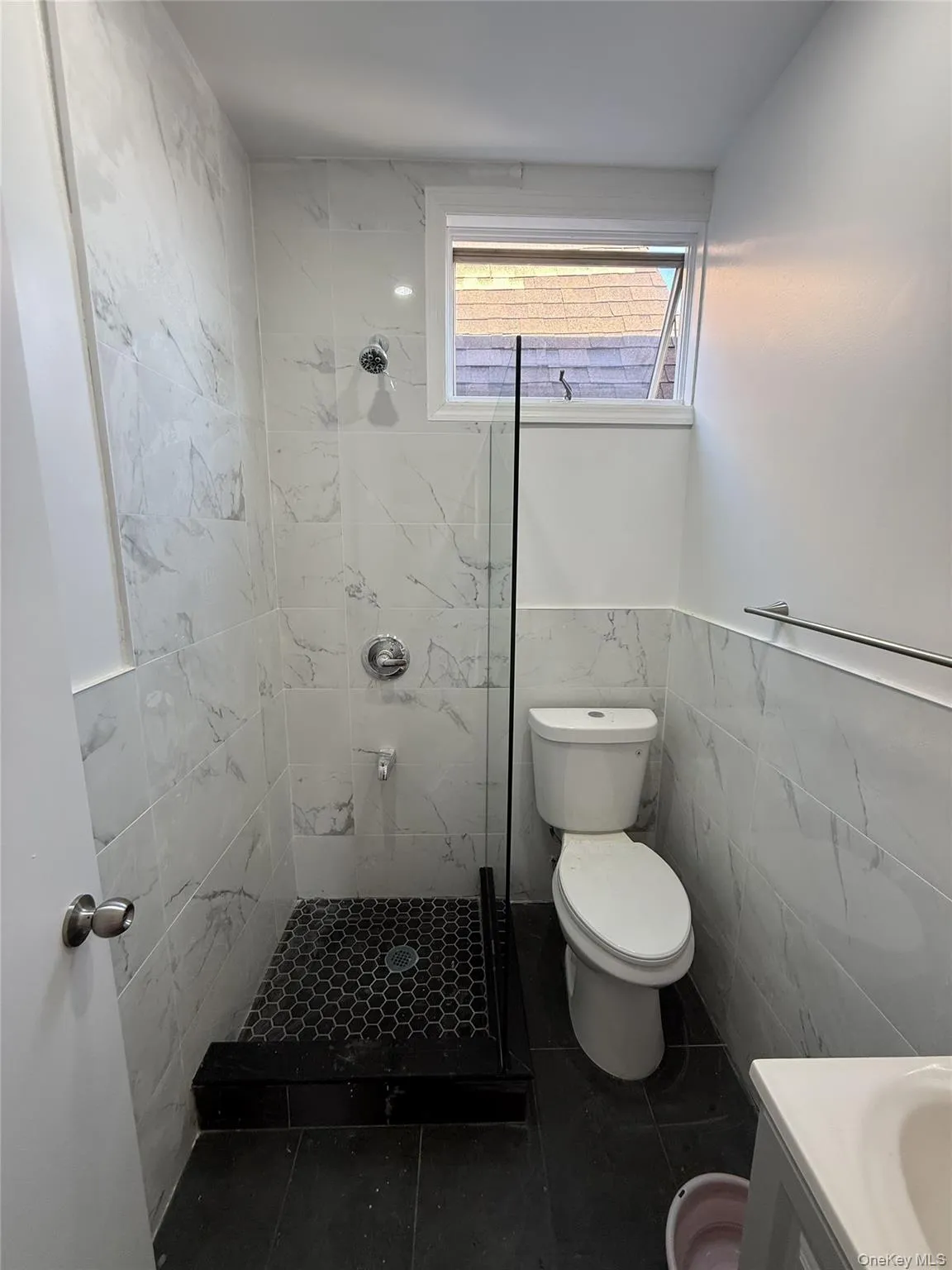 Bathroom featuring a shower with white marble-look wall tiling and a black hexagonal floor Bathroom featuring a shower with white marble-look wall tiling and a black hexagonal floor