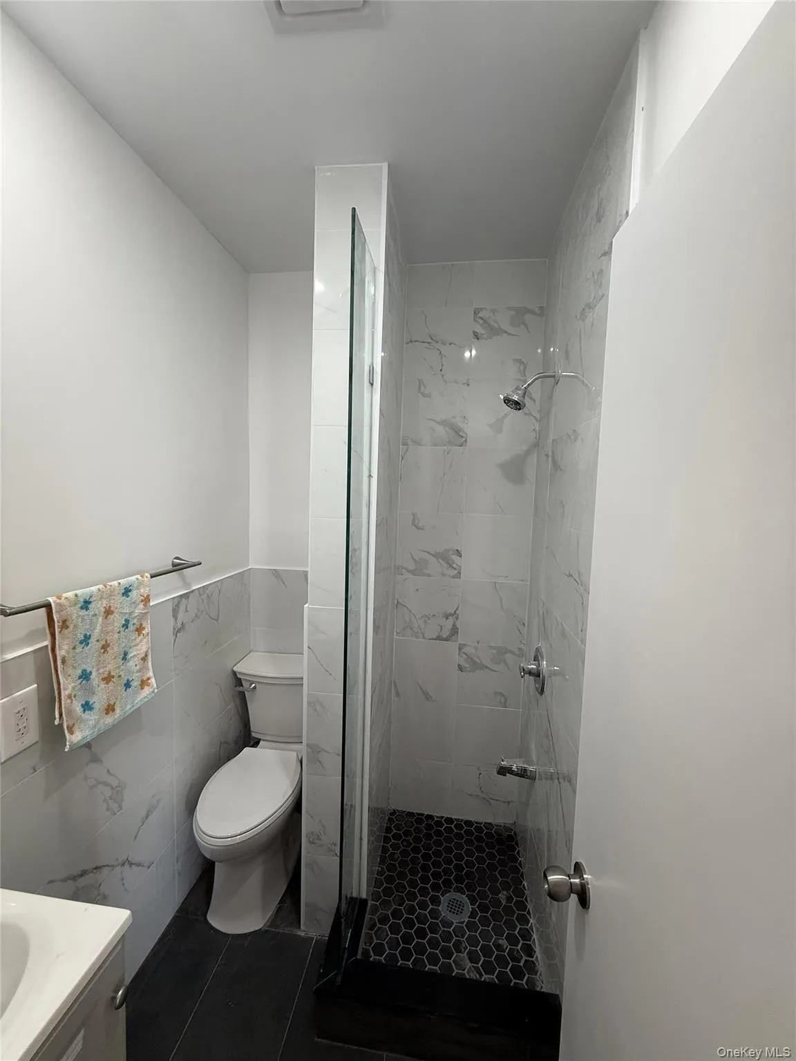 Walk-in shower with clear glass panel, hexagonal tile flooring, and white marble-look wall tiles Walk-in shower with clear glass panel, hexagonal tile flooring, and white marble-look wall tiles