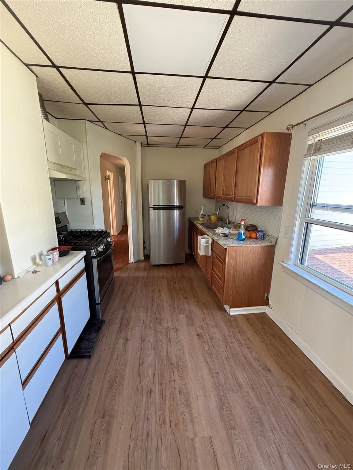 Kitchen featuring wood-finish flooring, stainless steel refrigerator, white and wood cabinetry, and a drop ceiling with integrated lighting Kitchen featuring wood-finish flooring, stainless steel refrigerator, white and wood cabinetry, and a drop ceiling with integrated lighting