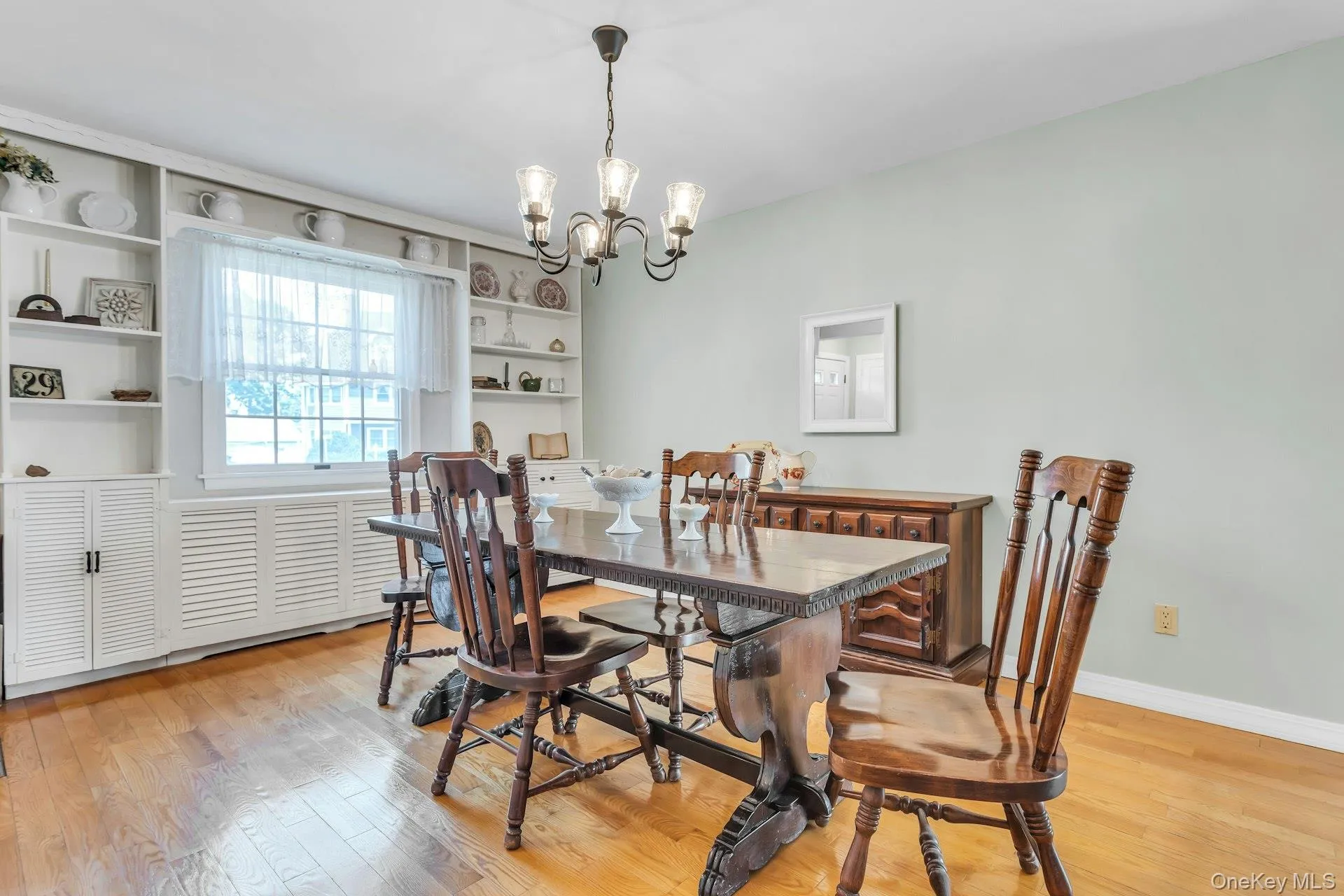 Dining area featuring wood-finish flooring, built-in shelving, window with natural light, and a prominent overhead chandelier Dining area featuring wood-finish flooring, built-in shelving, window with natural light, and a prominent overhead chandelier