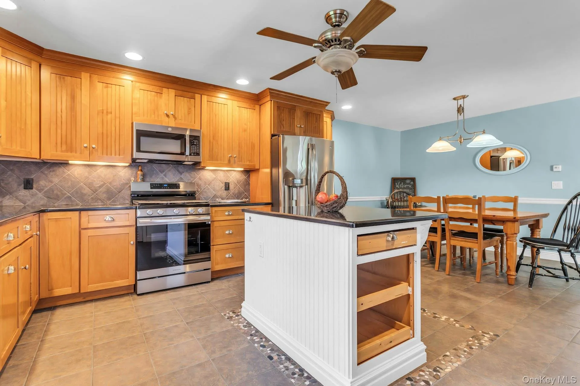 Kitchen featuring wood-finish cabinetry, stainless steel appliances, and dark countertops Kitchen featuring wood-finish cabinetry, stainless steel appliances, and dark countertops