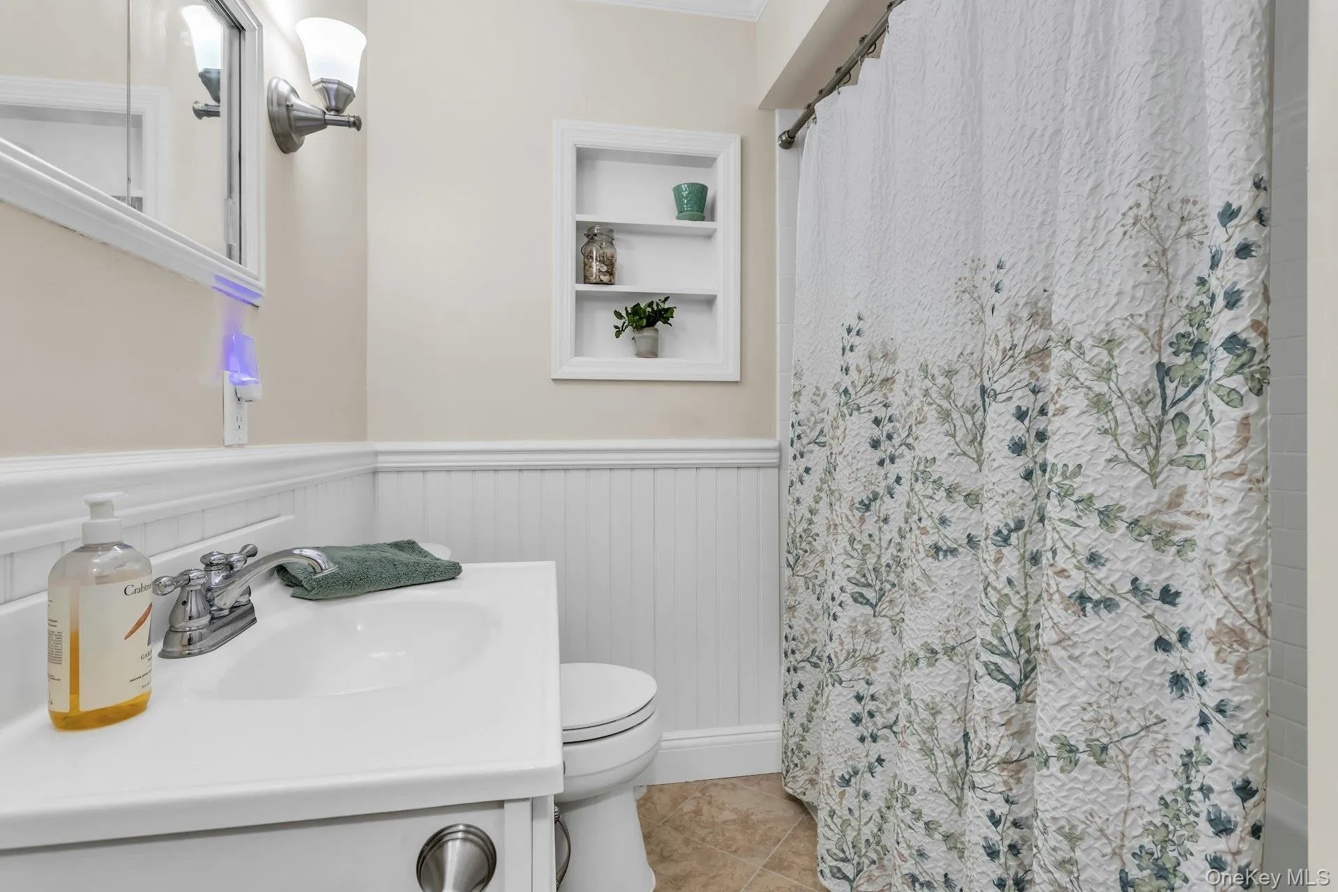 Bathroom featuring a white vanity with integrated sink, chrome faucet, wall-mounted mirror, and beadboard wainscoting Bathroom featuring a white vanity with integrated sink, chrome faucet, wall-mounted mirror, and beadboard wainscoting