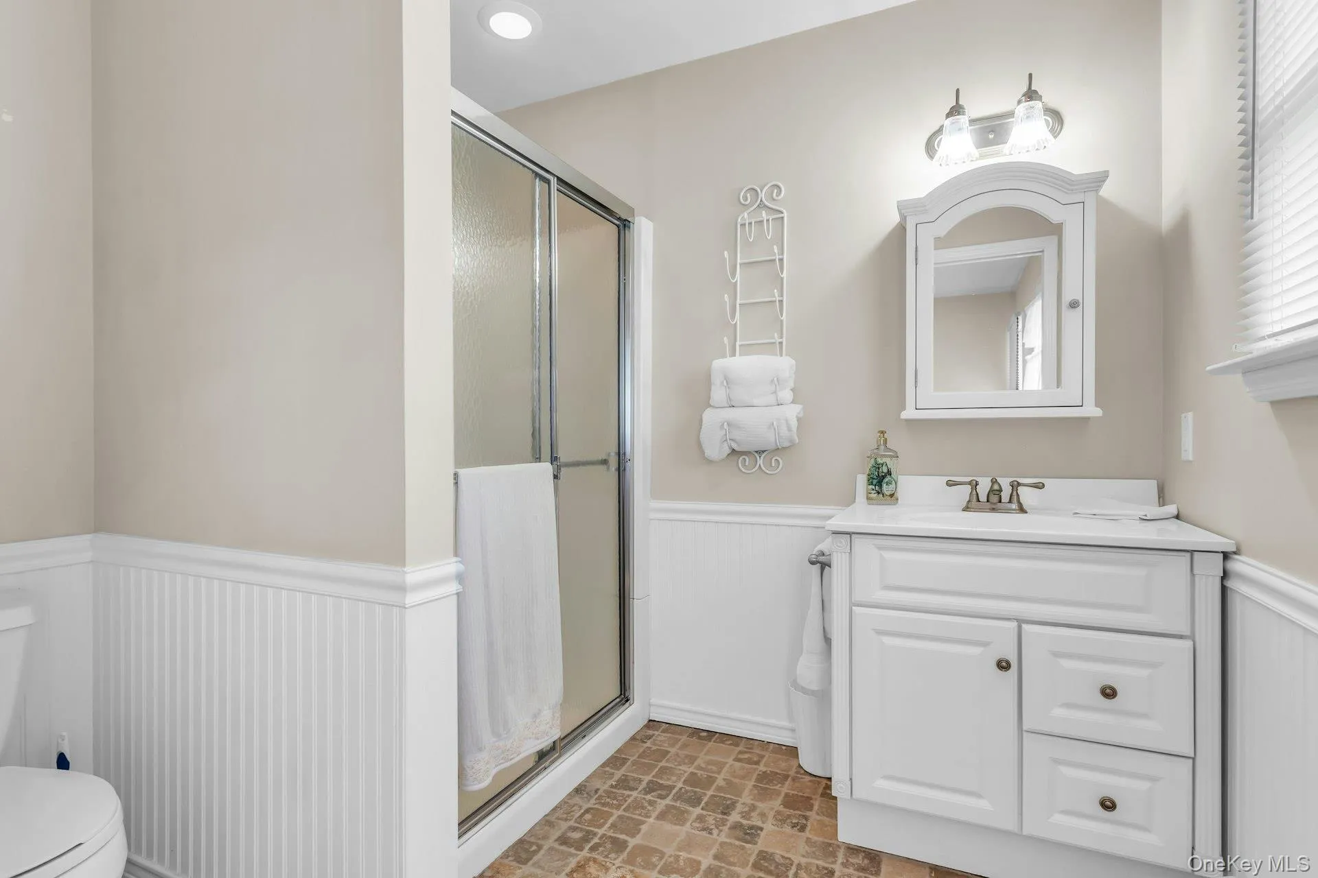Bathroom featuring a white vanity with integrated sink, a wall-mounted mirrored medicine cabinet, and a walk-in shower with a sliding glass door Bathroom featuring a white vanity with integrated sink, a wall-mounted mirrored medicine cabinet, and a walk-in shower with a sliding glass door