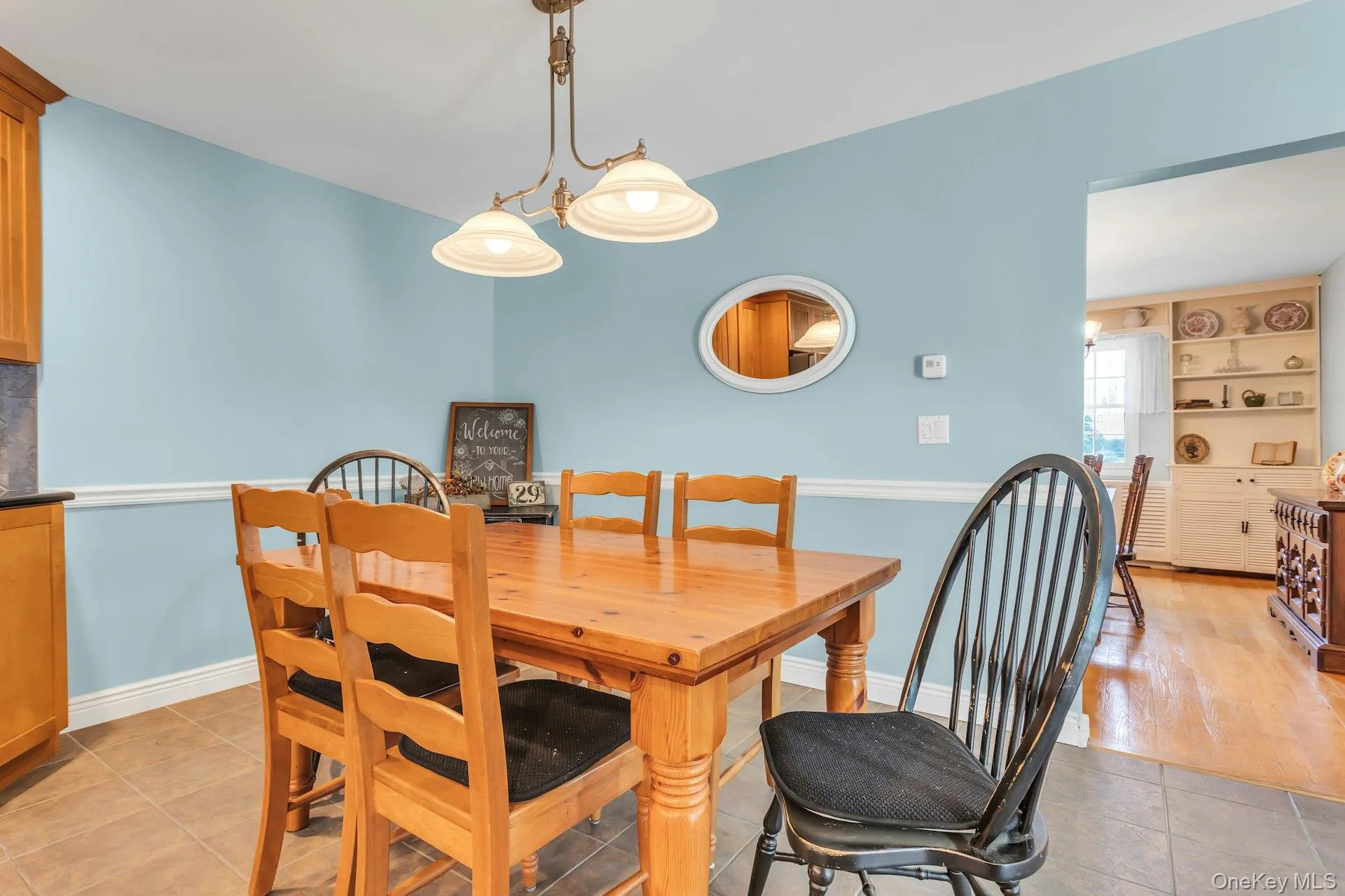 Dining area featuring tiled flooring, wainscoting detail, and a brass-finish chandelier with bell-shaped shades Dining area featuring tiled flooring, wainscoting detail, and a brass-finish chandelier with bell-shaped shades