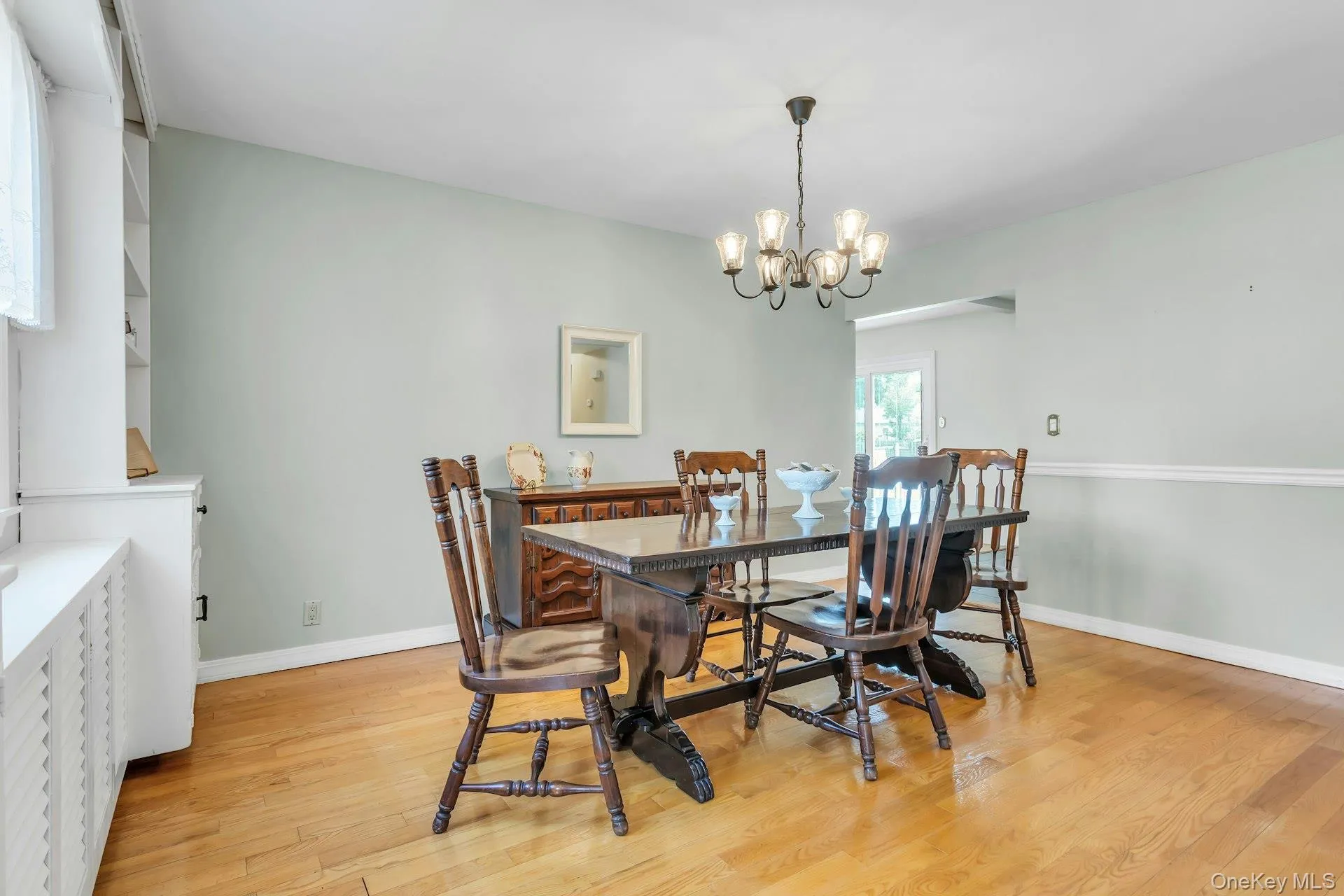 Spacious dining area featuring wood-finish flooring, a decorative chandelier, and white built-in shelving Spacious dining area featuring wood-finish flooring, a decorative chandelier, and white built-in shelving