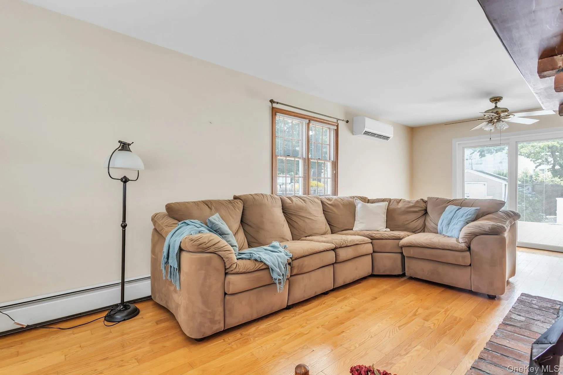 Living area featuring light wood-finish flooring, ample natural light from multiple windows, a ceiling fan, and a mini-split HVAC unit Living area featuring light wood-finish flooring, ample natural light from multiple windows, a ceiling fan, and a mini-split HVAC unit