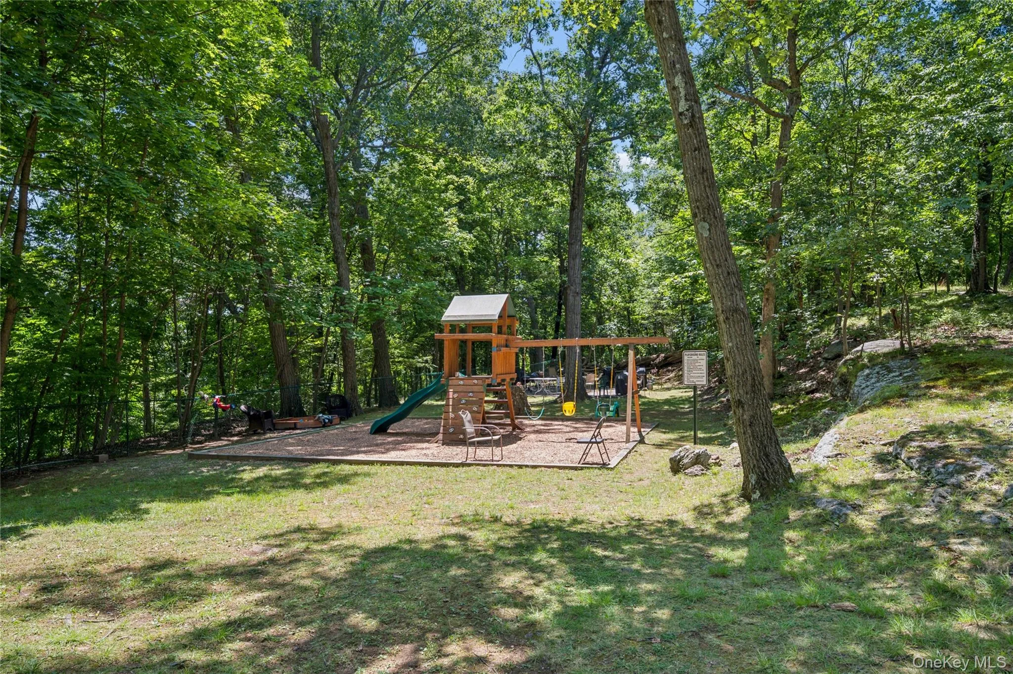 Wood-toned playset with multiple swings and a green slide, set on a wood chip base Wood-toned playset with multiple swings and a green slide, set on a wood chip base