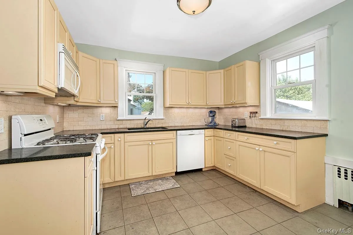 Kitchen featuring ample cabinetry, dark countertops, a tile backsplash, and tile flooring Kitchen featuring ample cabinetry, dark countertops, a tile backsplash, and tile flooring