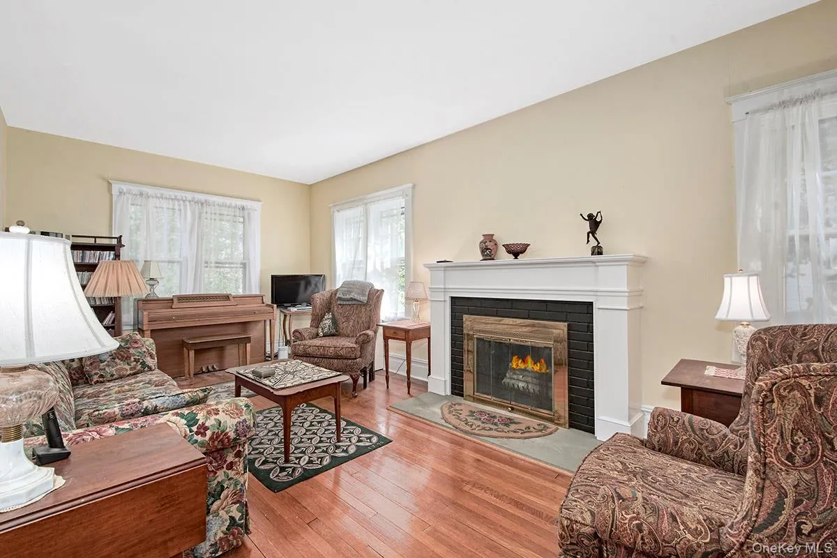 Living room featuring hardwood floors, a white mantel fireplace with black brick surround, and multiple windows Living room featuring hardwood floors, a white mantel fireplace with black brick surround, and multiple windows