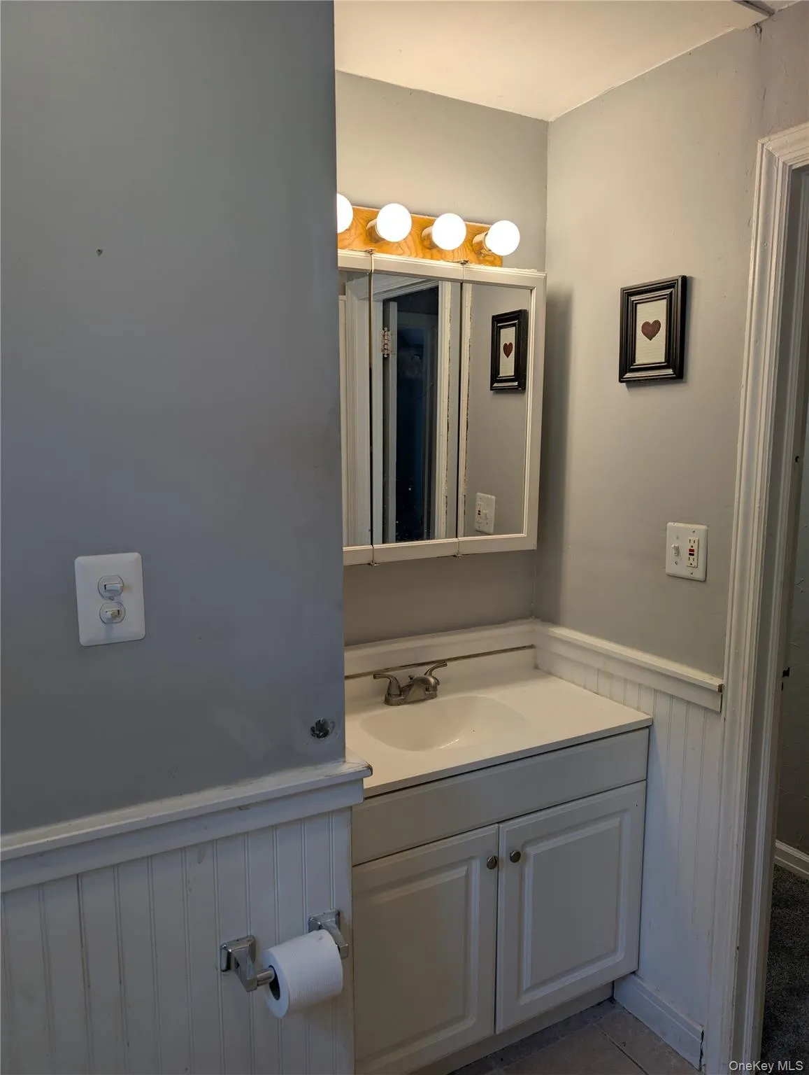 Bathroom features a single vanity with integrated sink, white cabinetry, and beadboard wainscoting Bathroom features a single vanity with integrated sink, white cabinetry, and beadboard wainscoting