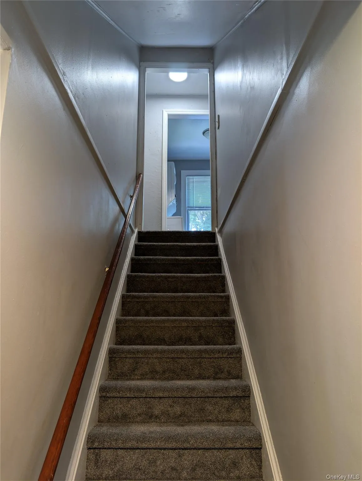 Carpeted staircase features a wooden handrail and neutral wall tones Carpeted staircase features a wooden handrail and neutral wall tones