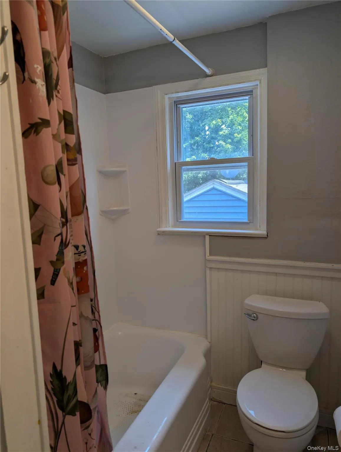 White bathtub with integrated shelving, a single-pane window, and a toilet with beadboard wainscoting White bathtub with integrated shelving, a single-pane window, and a toilet with beadboard wainscoting