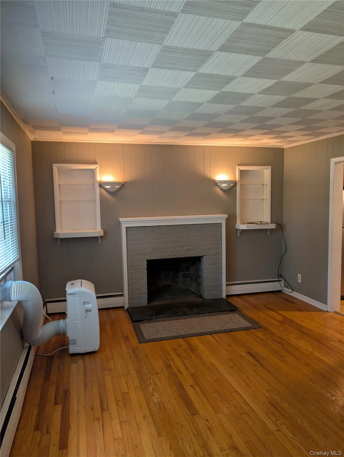 Living area featuring wood-finish flooring and a decorative central fireplace with a stone hearth, bookshelves and sconces Living area featuring wood-finish flooring and a decorative central fireplace with a stone hearth, bookshelves and sconces