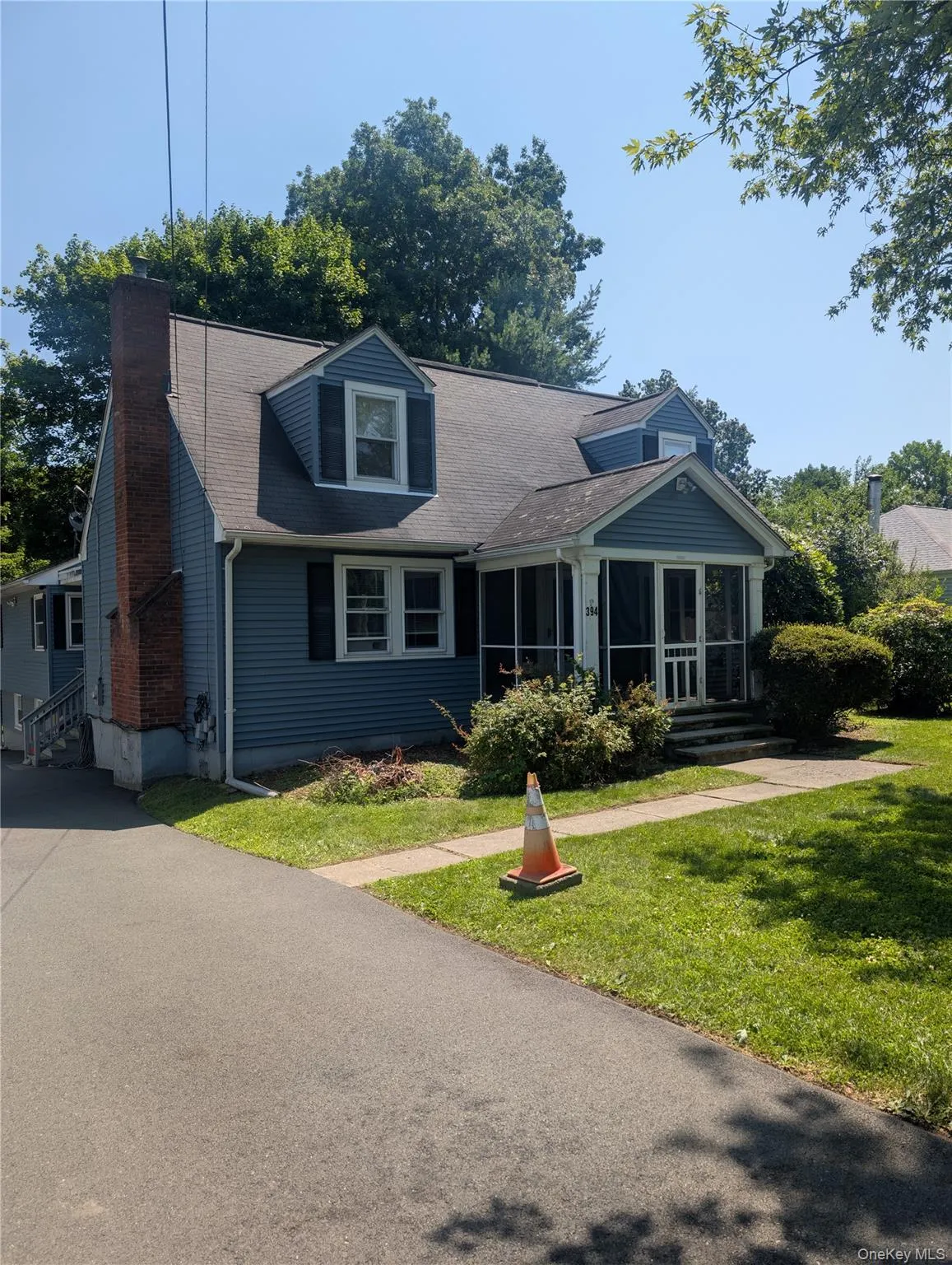 Dormered Cape Cod features blue siding, a screened-in porch, a brick chimney, and a paved driveway Dormered Cape Cod features blue siding, a screened-in porch, a brick chimney, and a paved driveway