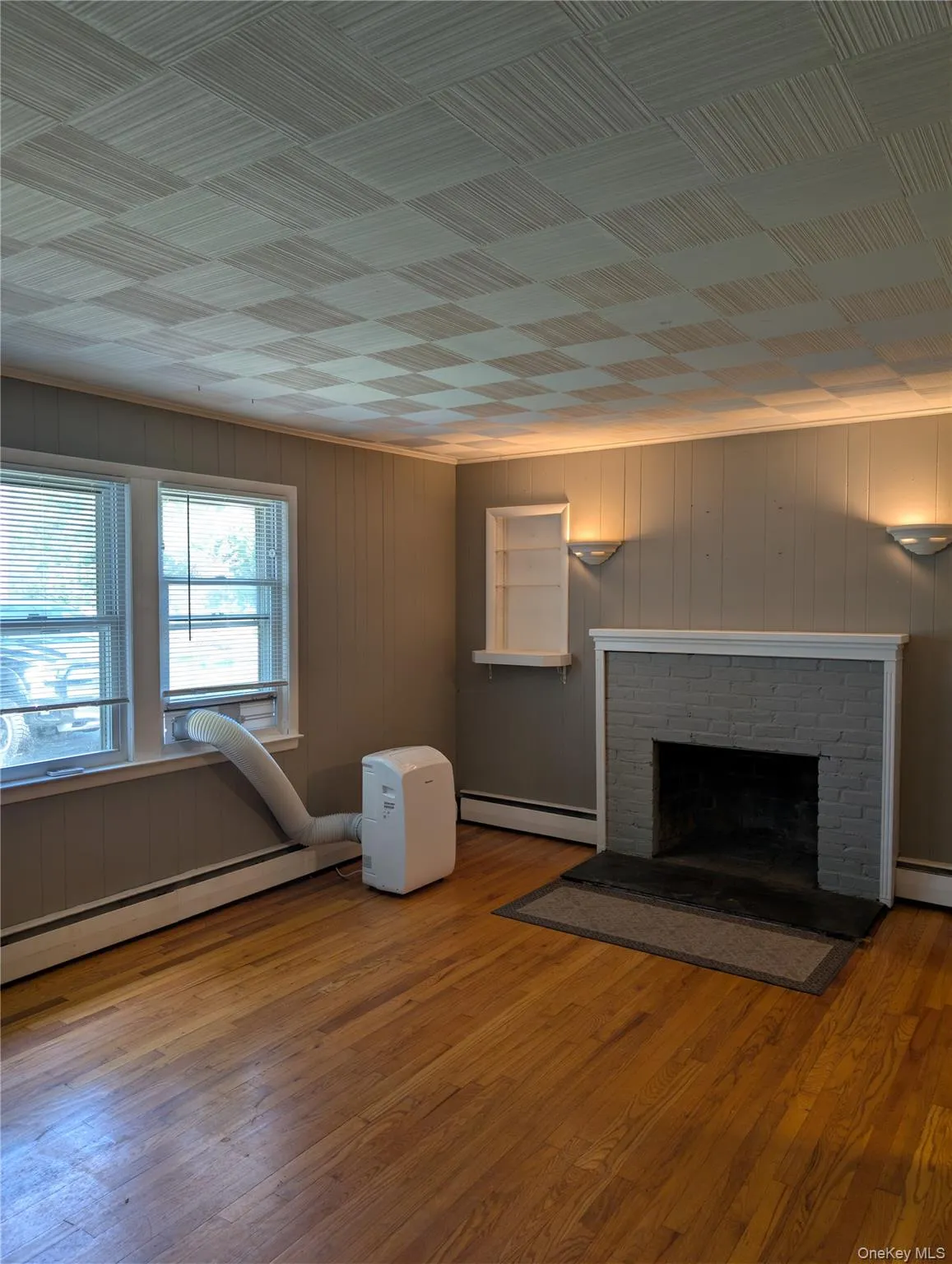 Hardwood flooring throughout features a decorative brick fireplace with a painted mantel, built-in shelving, and wall sconces and dual windows Hardwood flooring throughout features a decorative brick fireplace with a painted mantel, built-in shelving, and wall sconces and dual windows