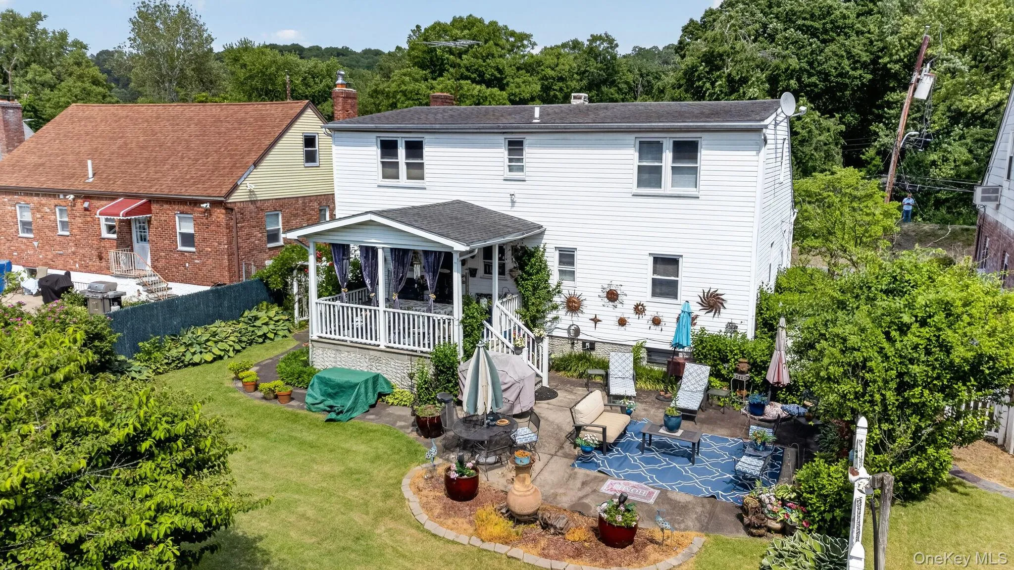 Rear exterior featuring a covered porch with white railing, a stone patio, and a terraced garden bed Rear exterior featuring a covered porch with white railing, a stone patio, and a terraced garden bed