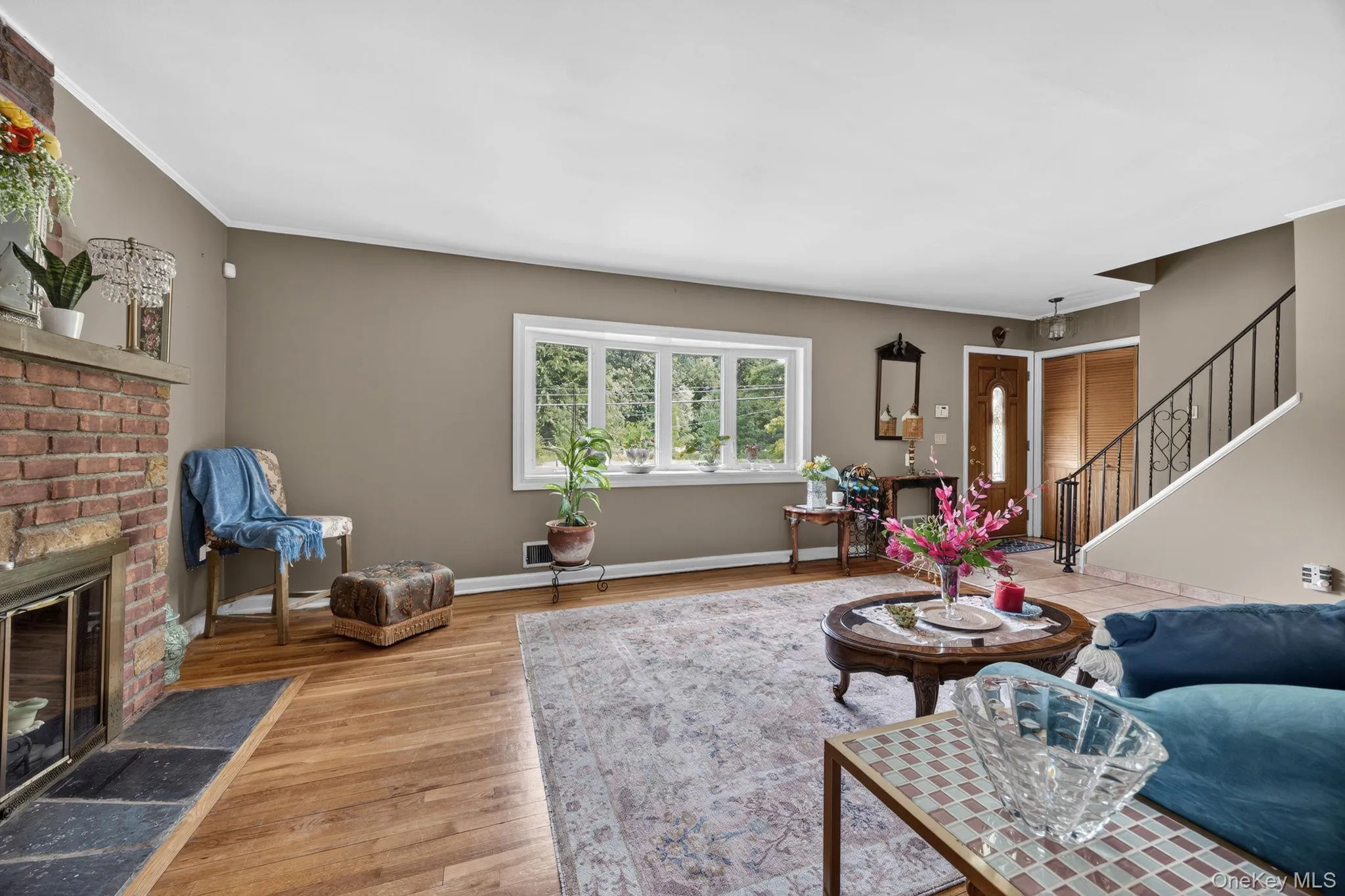 Living room featuring wood-finish flooring, a bay window, and a brick fireplace with a stone hearth Living room featuring wood-finish flooring, a bay window, and a brick fireplace with a stone hearth