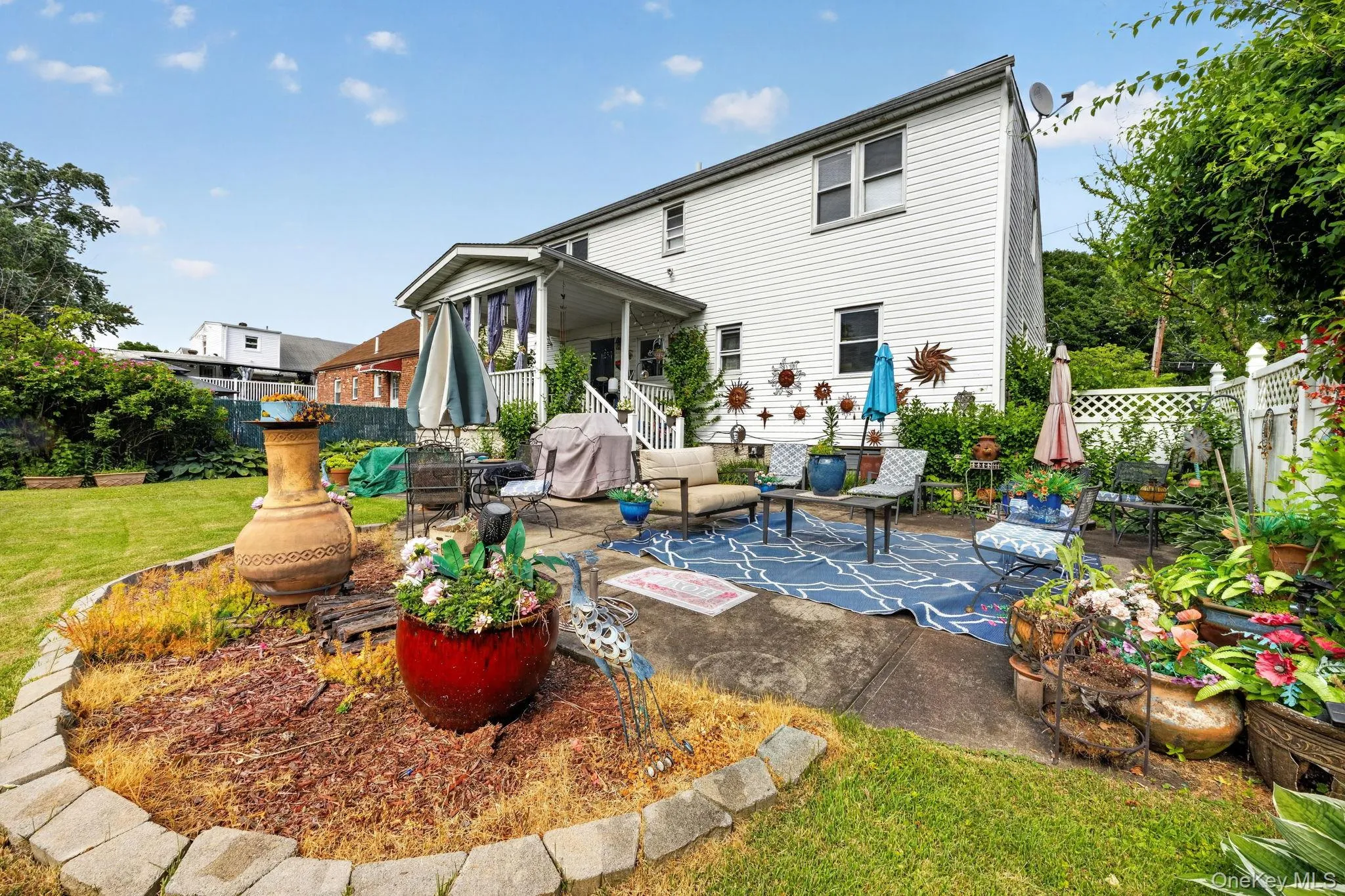 Expansive backyard featuring a concrete patio, mature landscaping, and a white lattice fence Expansive backyard featuring a concrete patio, mature landscaping, and a white lattice fence