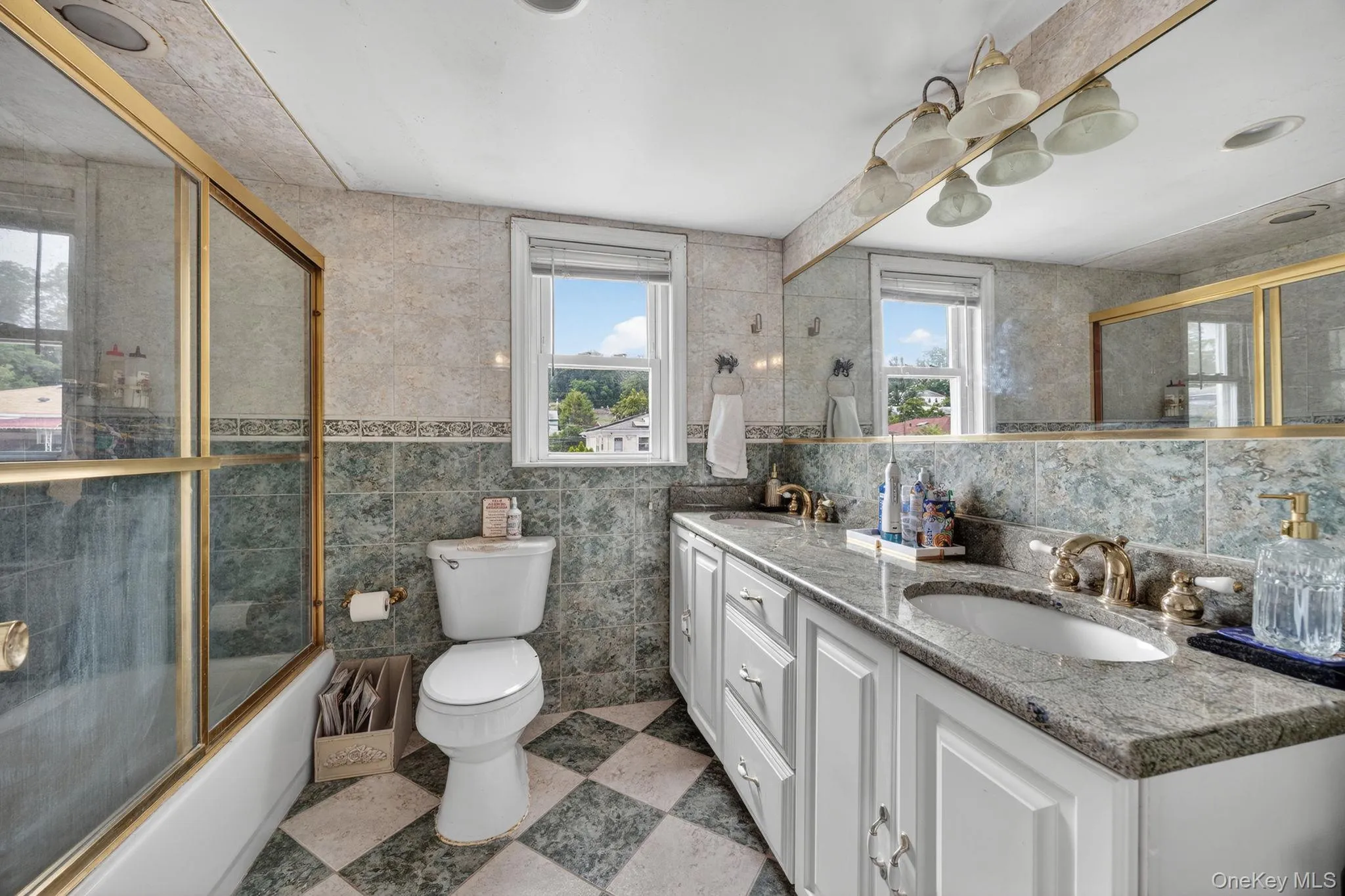 Bathroom featuring a dual vanity with granite countertops, tile flooring, built-in bathtub with glass enclosure, and tiled walls Bathroom featuring a dual vanity with granite countertops, tile flooring, built-in bathtub with glass enclosure, and tiled walls