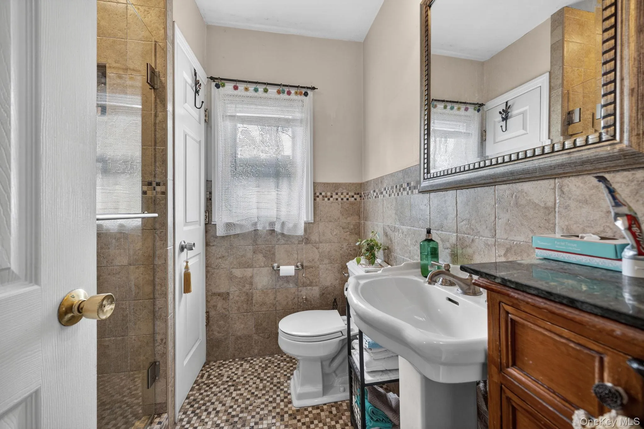 Bathroom featuring a neutral tile shower with a glass enclosure, a white pedestal sink with a chrome faucet, and a large decorative wall mirror Bathroom featuring a neutral tile shower with a glass enclosure, a white pedestal sink with a chrome faucet, and a large decorative wall mirror