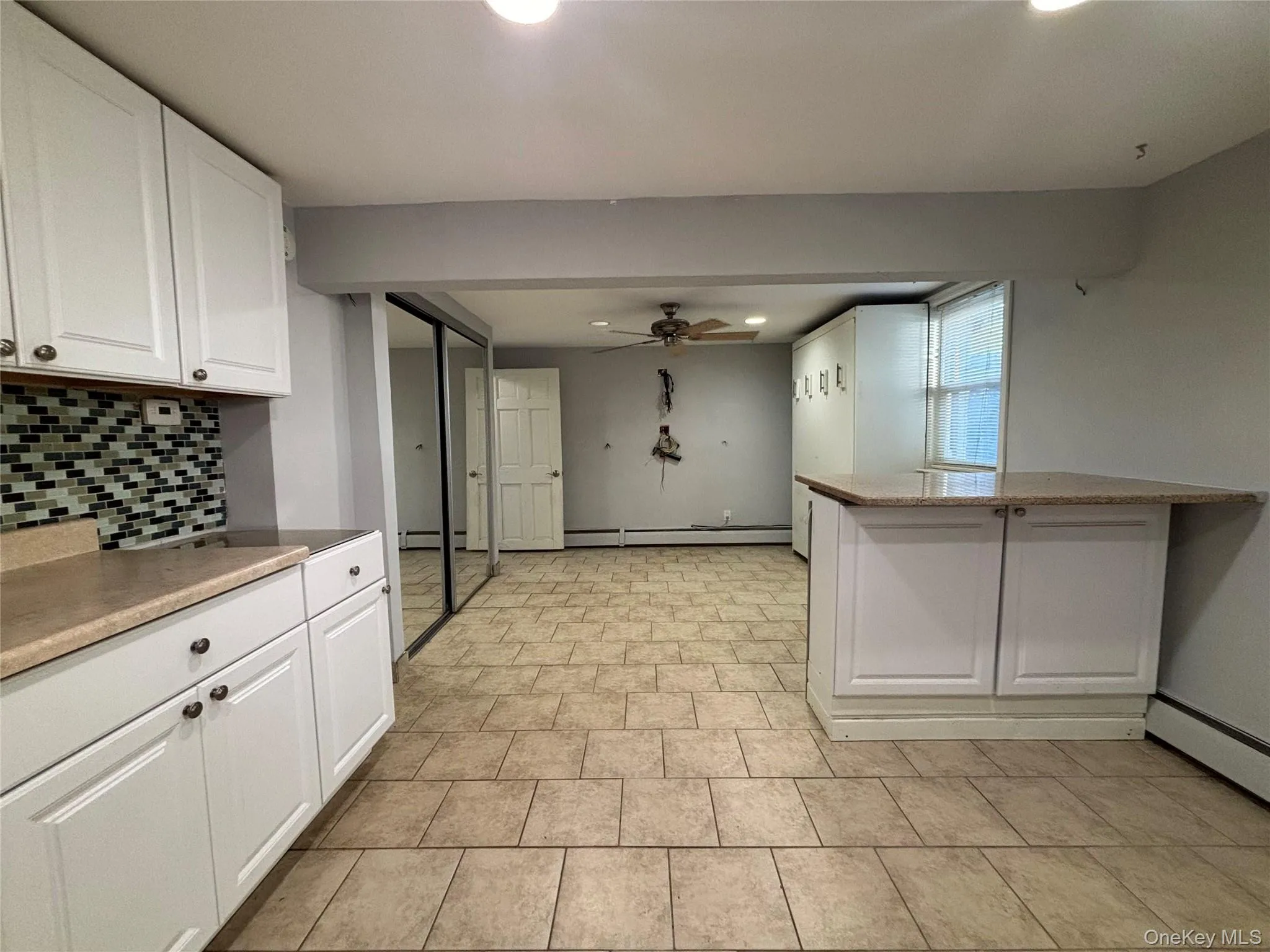 Open-concept space featuring white cabinetry with brushed nickel hardware, a mosaic tile backsplash, and light-toned countertops Open-concept space featuring white cabinetry with brushed nickel hardware, a mosaic tile backsplash, and light-toned countertops