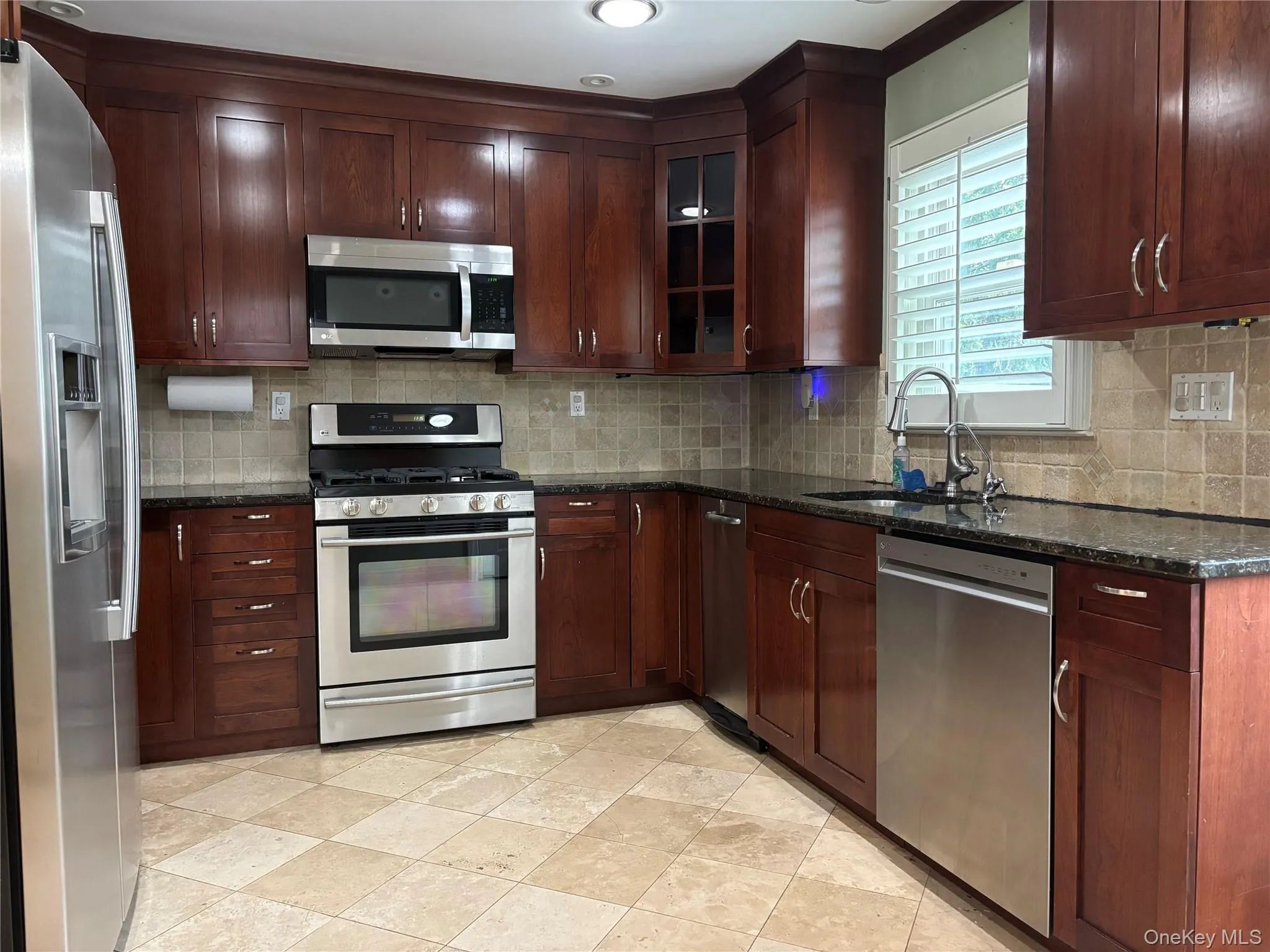 Kitchen featuring extensive dark wood cabinetry, stainless steel appliances, granite countertops, and a tiled backsplash Kitchen featuring extensive dark wood cabinetry, stainless steel appliances, granite countertops, and a tiled backsplash