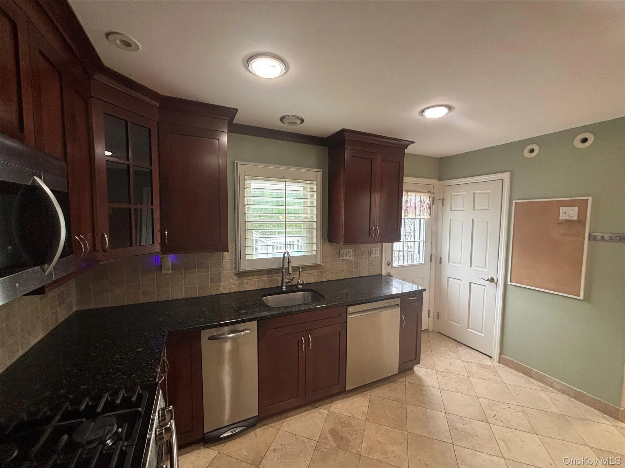 Kitchen featuring dark wood cabinetry, stainless steel appliances, dark stone countertops, tile backsplash, and ceramic tile flooring Kitchen featuring dark wood cabinetry, stainless steel appliances, dark stone countertops, tile backsplash, and ceramic tile flooring