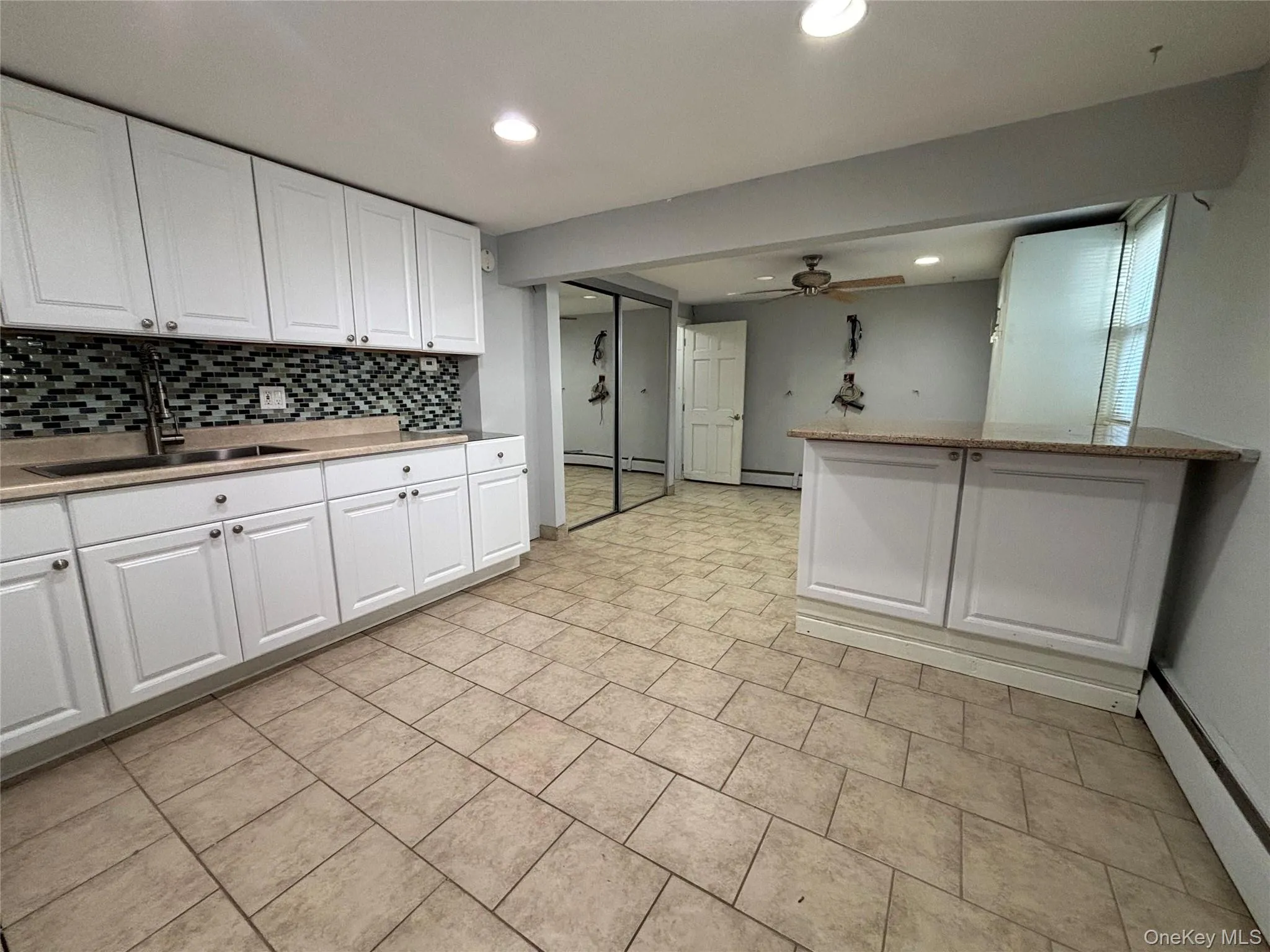 Kitchenette featuring white cabinetry, a stainless steel sink, and a mosaic tile backsplash Kitchenette featuring white cabinetry, a stainless steel sink, and a mosaic tile backsplash