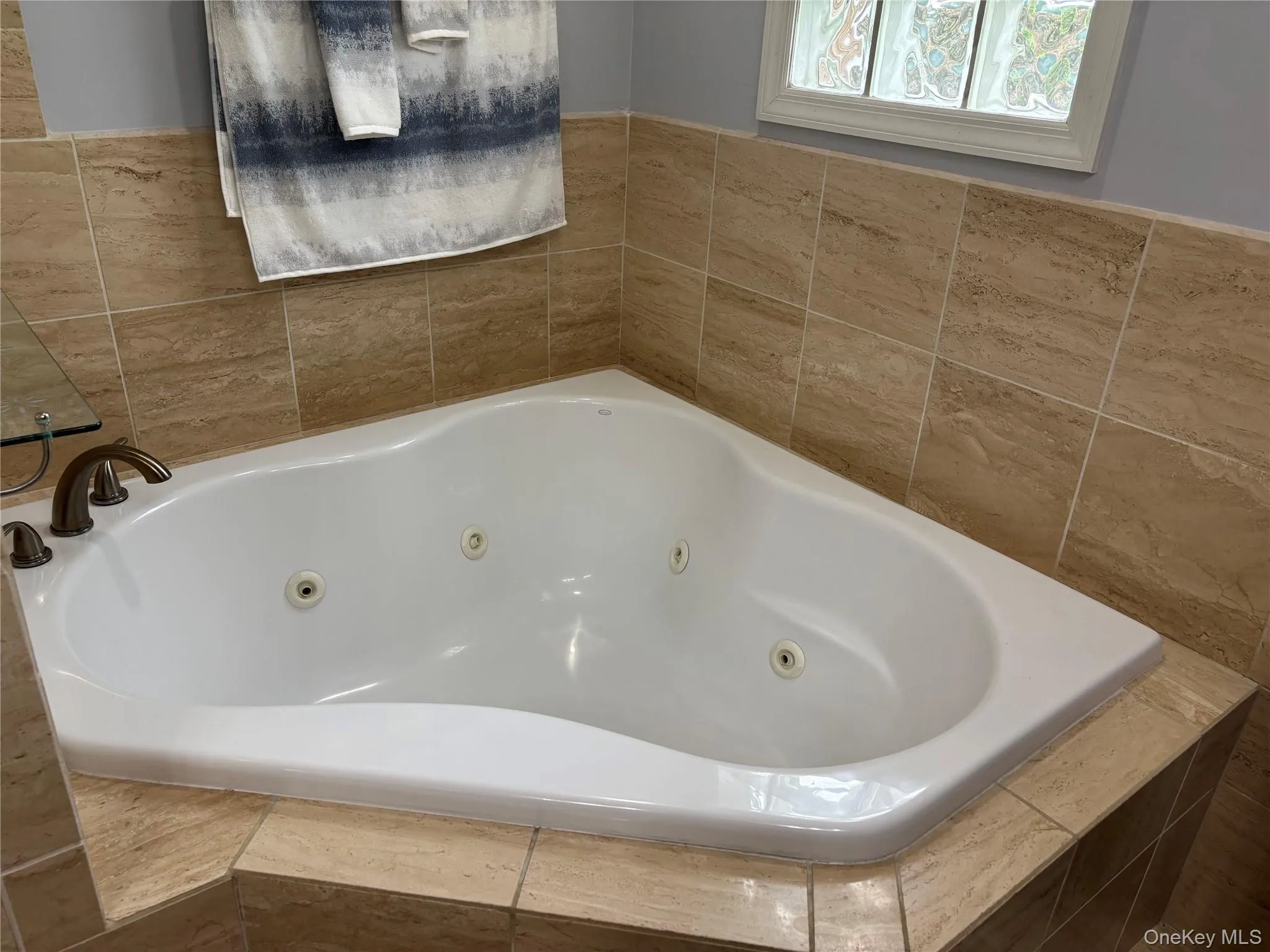 Corner jetted tub with bronze-finish fixtures, surrounded by earth-tone tile walls and a coordinating tile deck Corner jetted tub with bronze-finish fixtures, surrounded by earth-tone tile walls and a coordinating tile deck