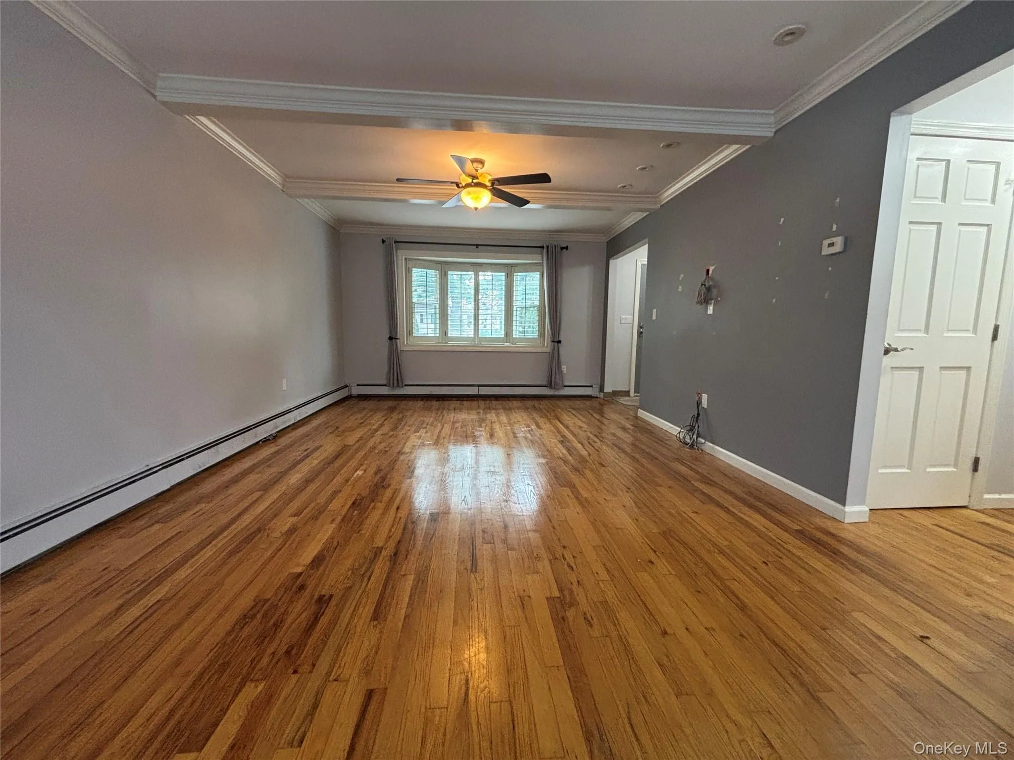 Spacious interior with wood-finish flooring, bay window, white trim, and a ceiling fan Spacious interior with wood-finish flooring, bay window, white trim, and a ceiling fan