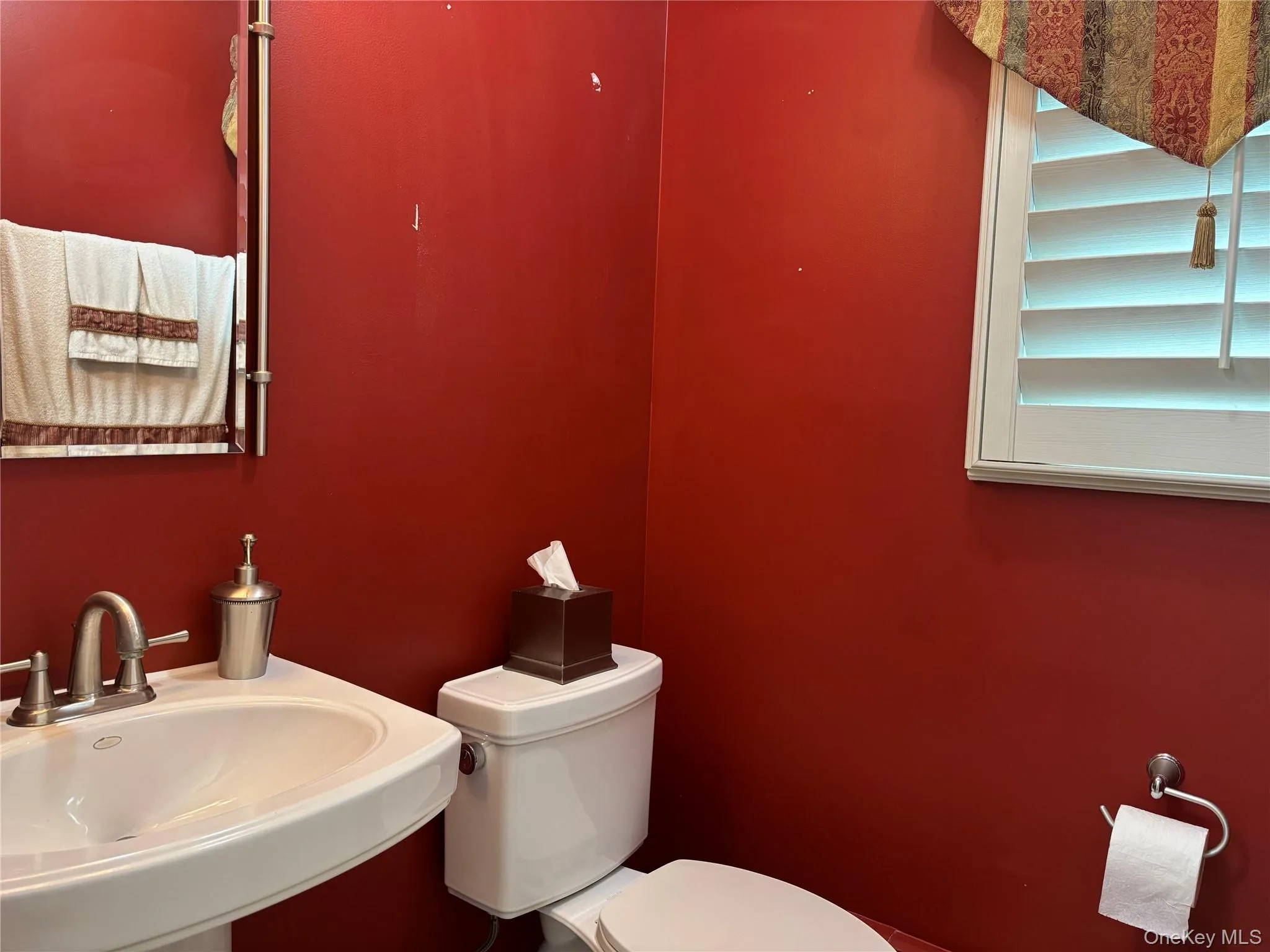 Pedestal sink with brushed nickel faucet, mirror with integrated towel bar, and white louvered window shutters Pedestal sink with brushed nickel faucet, mirror with integrated towel bar, and white louvered window shutters