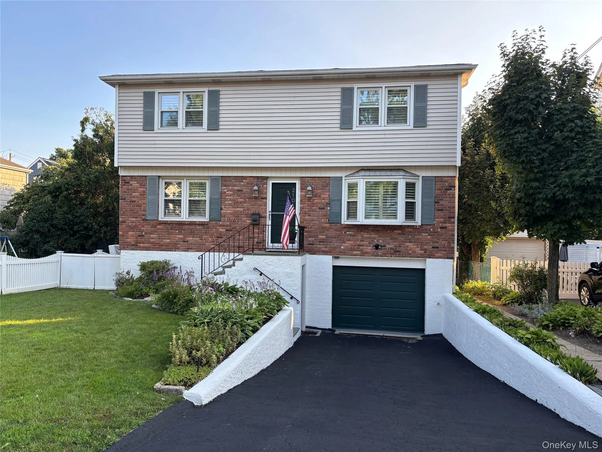 Split-level residence featuring brick and siding facade, a bay window, and a dark green garage door Split-level residence featuring brick and siding facade, a bay window, and a dark green garage door