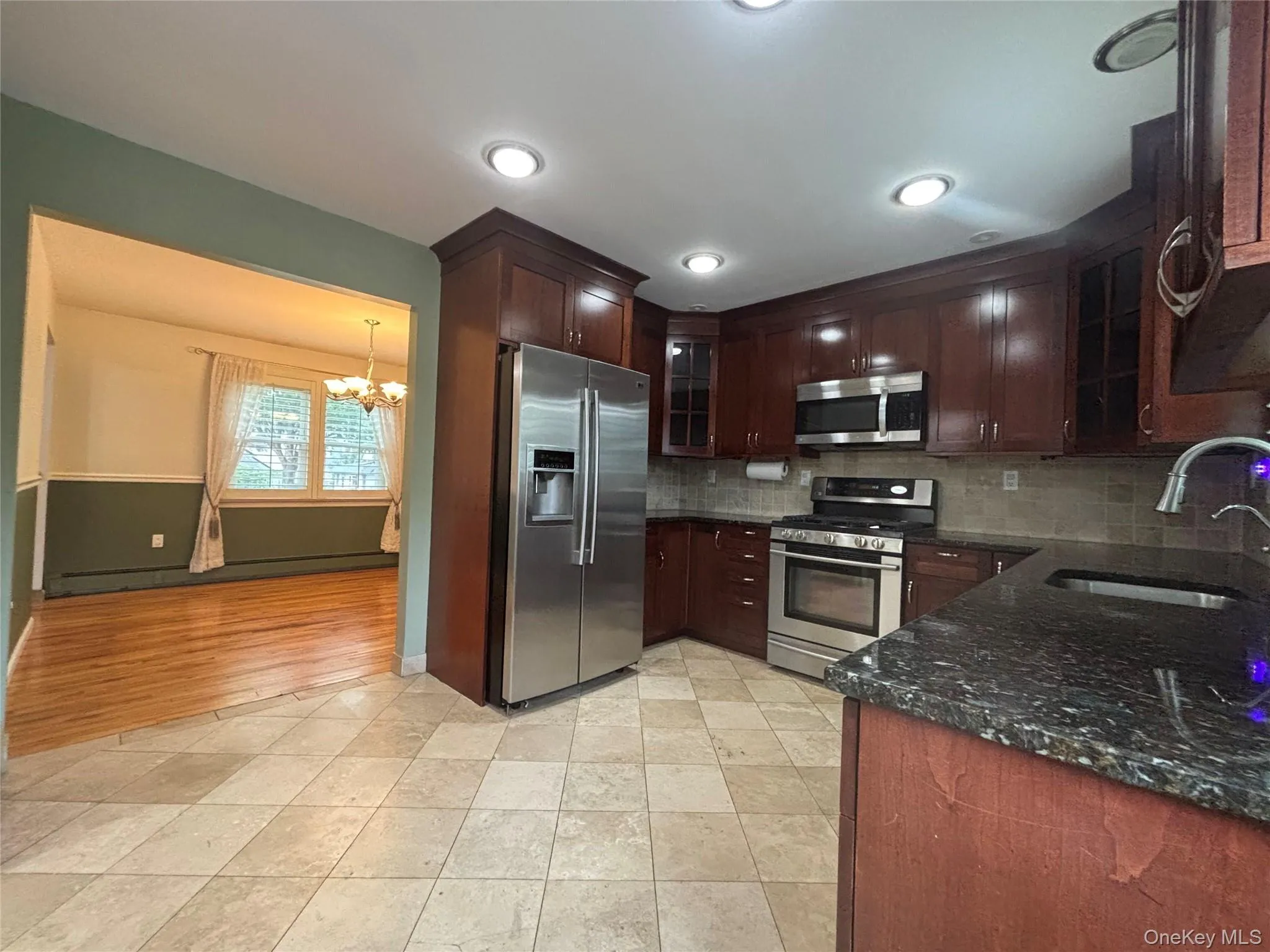 Kitchen featuring tile flooring, dark wood cabinetry, granite countertops, and stainless steel appliances including a refrigerator, range, and microwave Kitchen featuring tile flooring, dark wood cabinetry, granite countertops, and stainless steel appliances including a refrigerator, range, and microwave