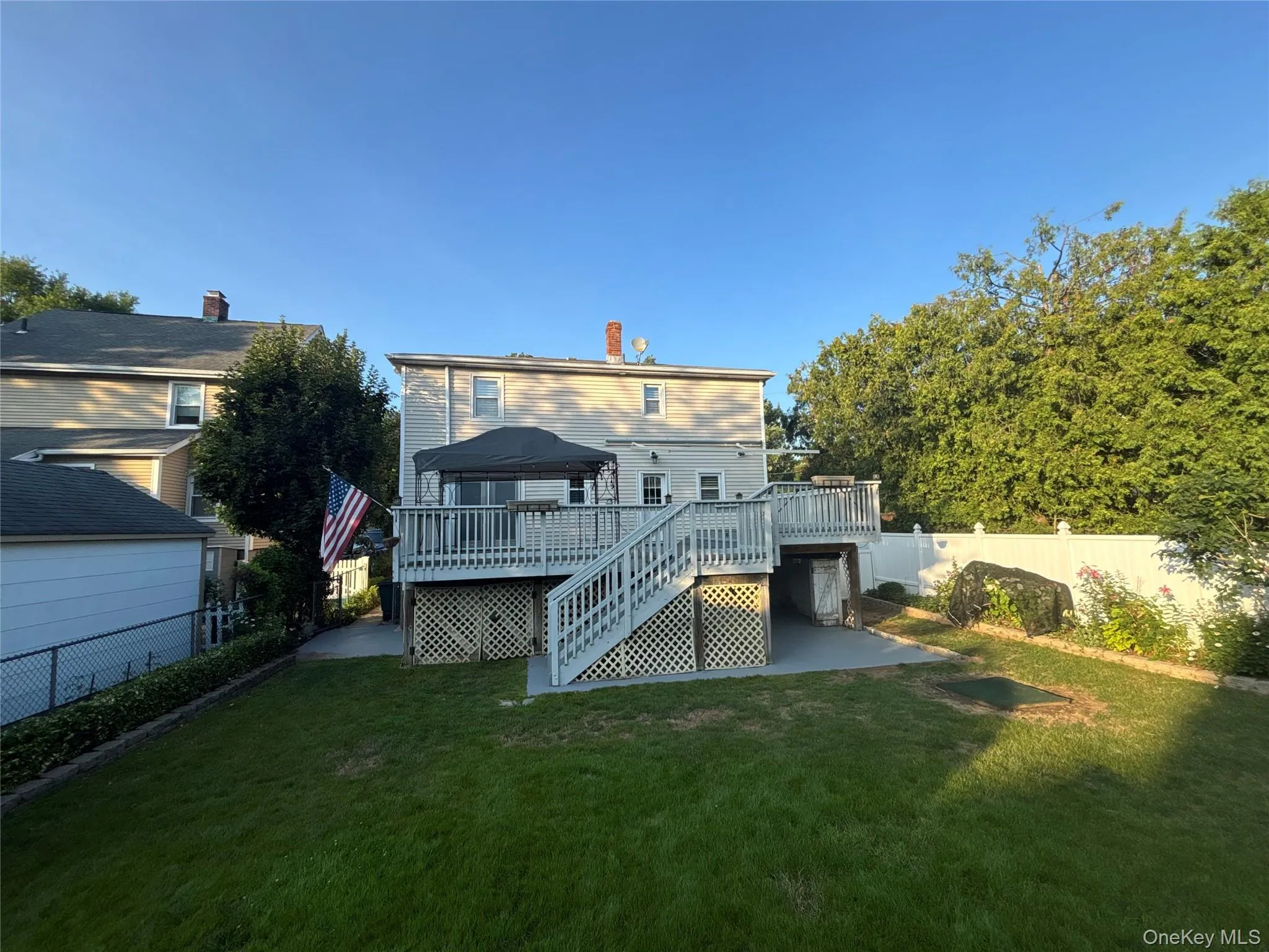 Expansive backyard featuring a manicured lawn, a multi-level wooden deck with lattice skirting, and a spacious concrete patio Expansive backyard featuring a manicured lawn, a multi-level wooden deck with lattice skirting, and a spacious concrete patio
