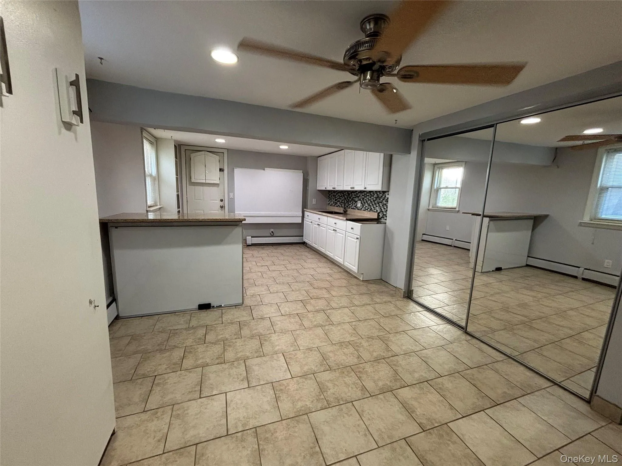 Spacious room featuring tile flooring, white cabinetry, a built-in bar with a stone-finish countertop, and full-wall mirrored closet doors Spacious room featuring tile flooring, white cabinetry, a built-in bar with a stone-finish countertop, and full-wall mirrored closet doors