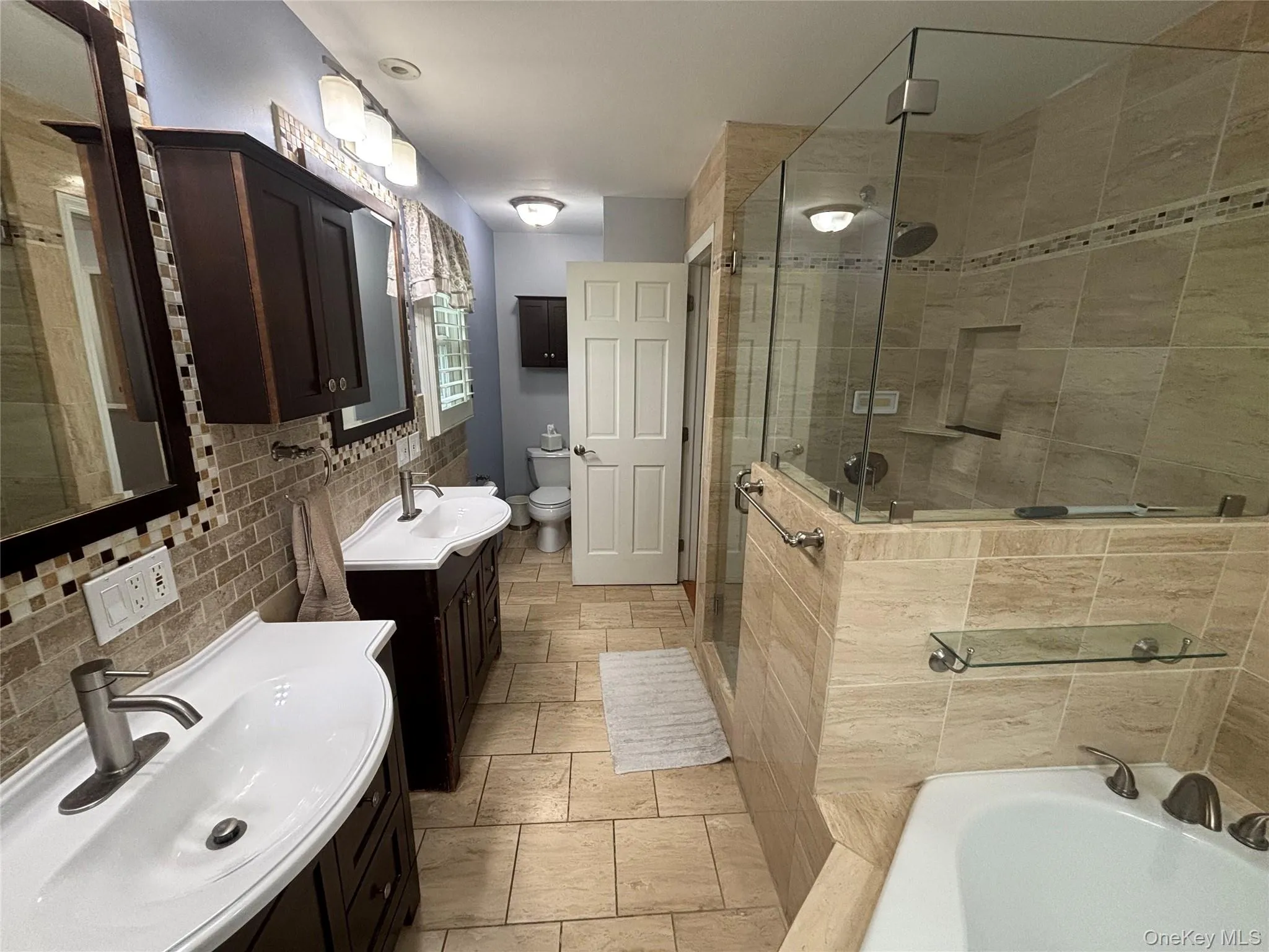 Bathroom featuring a glass-enclosed shower, built-in bathtub, and dual vanity sinks with dark wood-finish cabinetry Bathroom featuring a glass-enclosed shower, built-in bathtub, and dual vanity sinks with dark wood-finish cabinetry