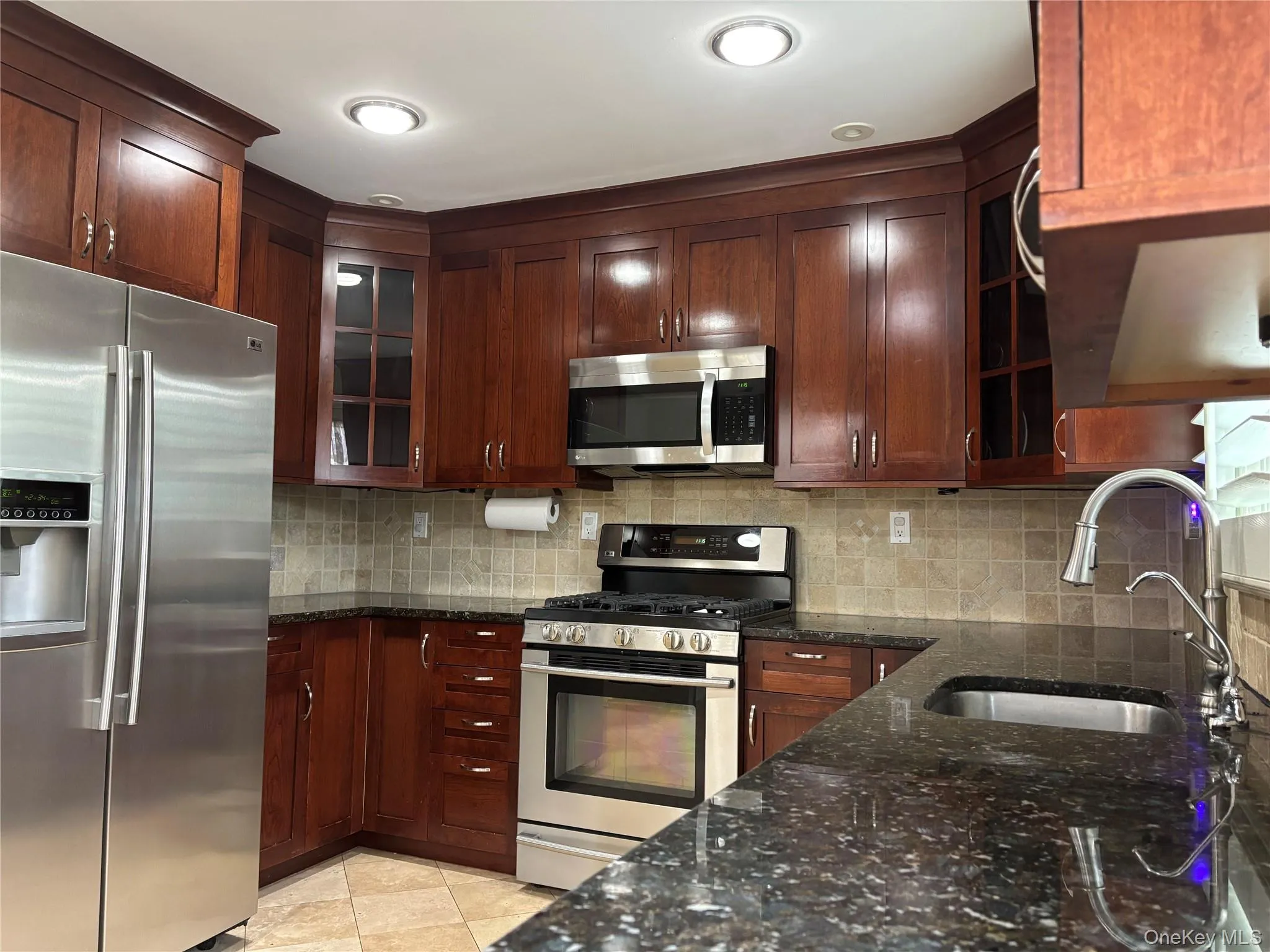 Kitchen featuring rich wood cabinetry, stainless steel appliances, dark speckled countertops, a tile backsplash, and recessed lighting Kitchen featuring rich wood cabinetry, stainless steel appliances, dark speckled countertops, a tile backsplash, and recessed lighting