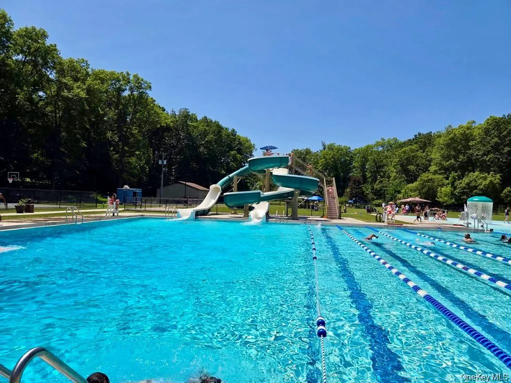 Expansive aquatic facility featuring a multi-lane swimming pool with lane markers, a dedicated water slide structure, and surrounding green space Expansive aquatic facility featuring a multi-lane swimming pool with lane markers, a dedicated water slide structure, and surrounding green space