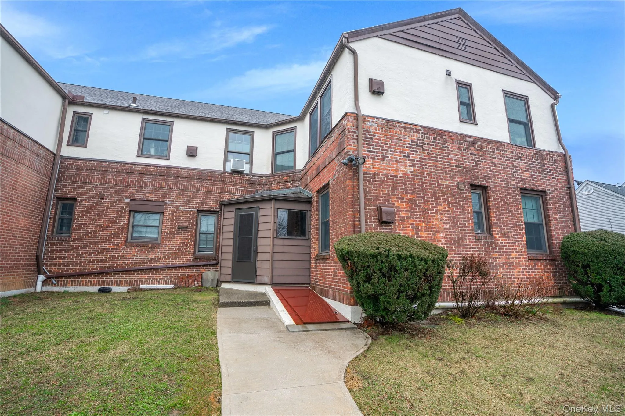 Brick and stucco exterior featuring multiple windows with dark trim, a screened-in porch with siding, and a concrete pathway Brick and stucco exterior featuring multiple windows with dark trim, a screened-in porch with siding, and a concrete pathway