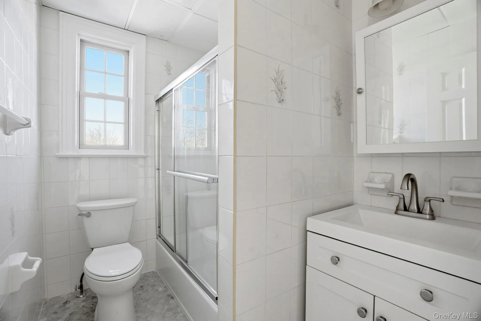 Bathroom featuring a white vanity with integrated sink, chrome faucet, wall-mounted medicine cabinet with mirror, and a window above the toilet Bathroom featuring a white vanity with integrated sink, chrome faucet, wall-mounted medicine cabinet with mirror, and a window above the toilet