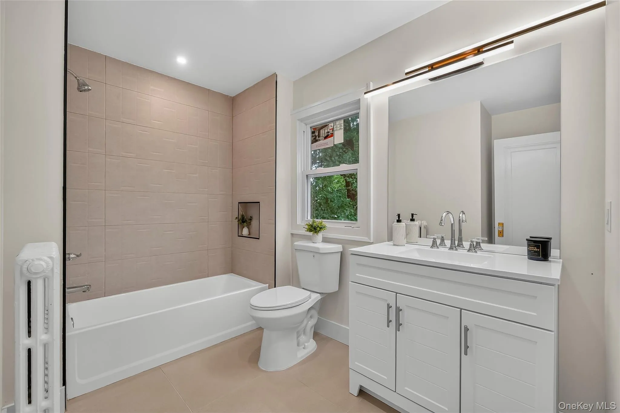 Bathroom featuring a white tub, textured beige tile surround with recessed niche, and a white vanity with an undermount sink and chrome fixtures Bathroom featuring a white tub, textured beige tile surround with recessed niche, and a white vanity with an undermount sink and chrome fixtures