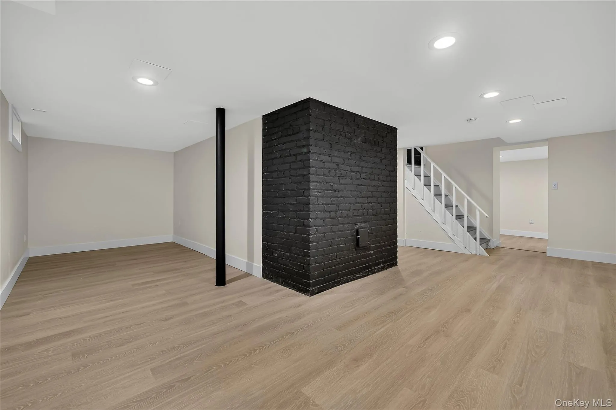Expansive finished basement featuring wood-finish flooring, recessed lighting, and a prominent black brick accent wall Expansive finished basement featuring wood-finish flooring, recessed lighting, and a prominent black brick accent wall
