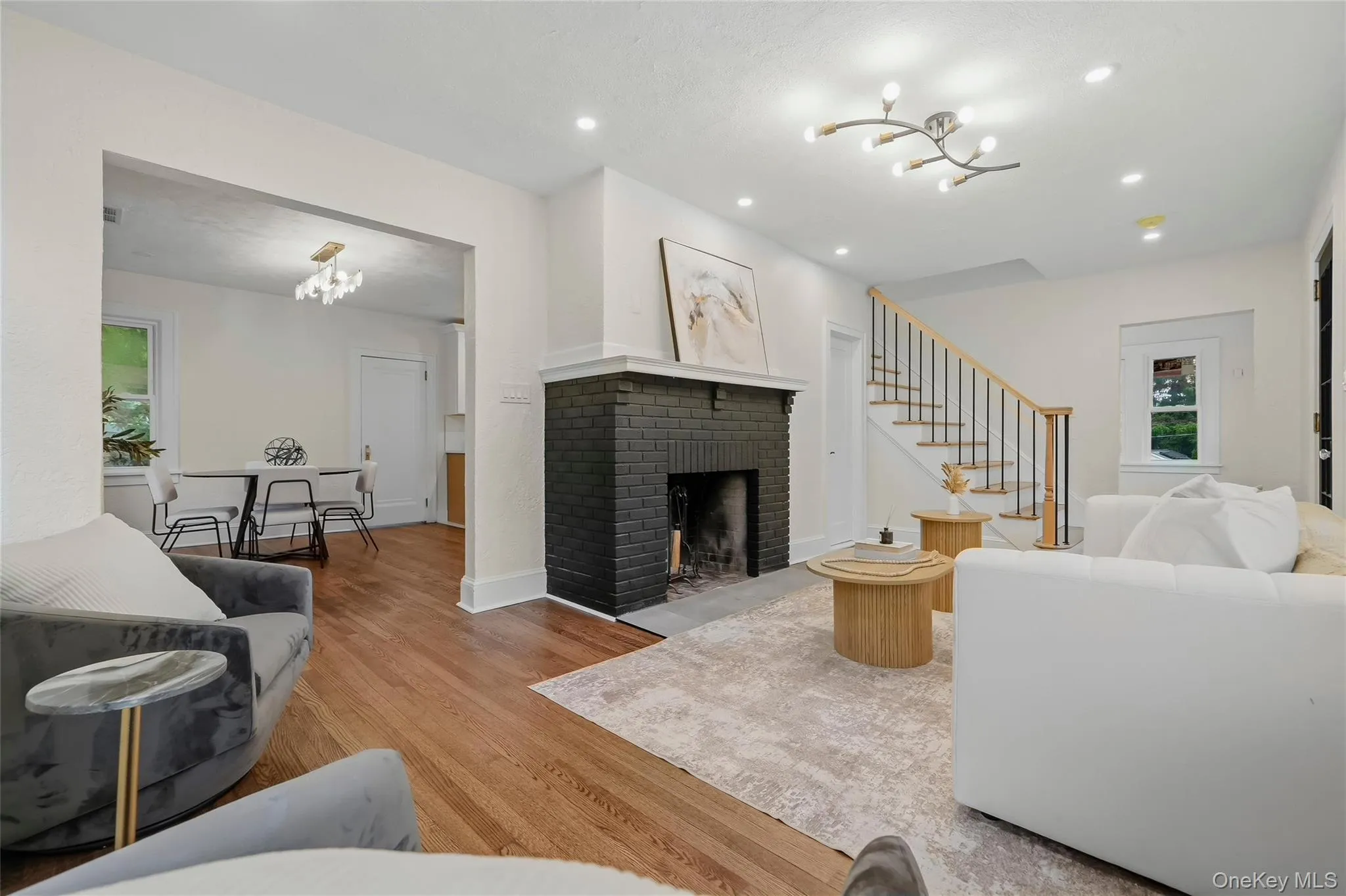 Living room featuring wood-finish flooring, a black brick fireplace, recessed lighting, and a modern ceiling light fixture Living room featuring wood-finish flooring, a black brick fireplace, recessed lighting, and a modern ceiling light fixture
