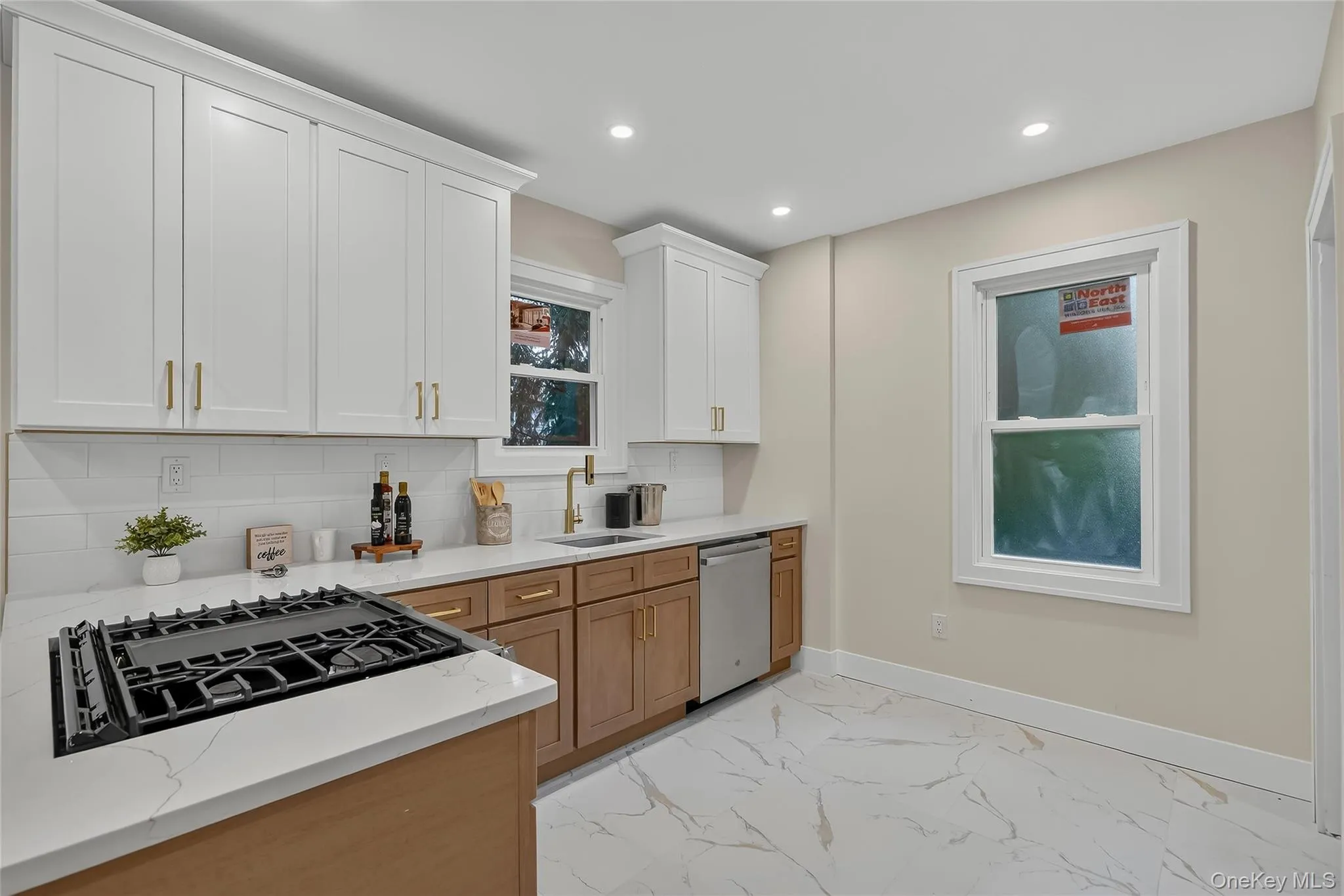 Modern kitchen featuring a gas cooktop, white upper cabinetry, natural wood-finish lower cabinetry, and light-toned countertops Modern kitchen featuring a gas cooktop, white upper cabinetry, natural wood-finish lower cabinetry, and light-toned countertops