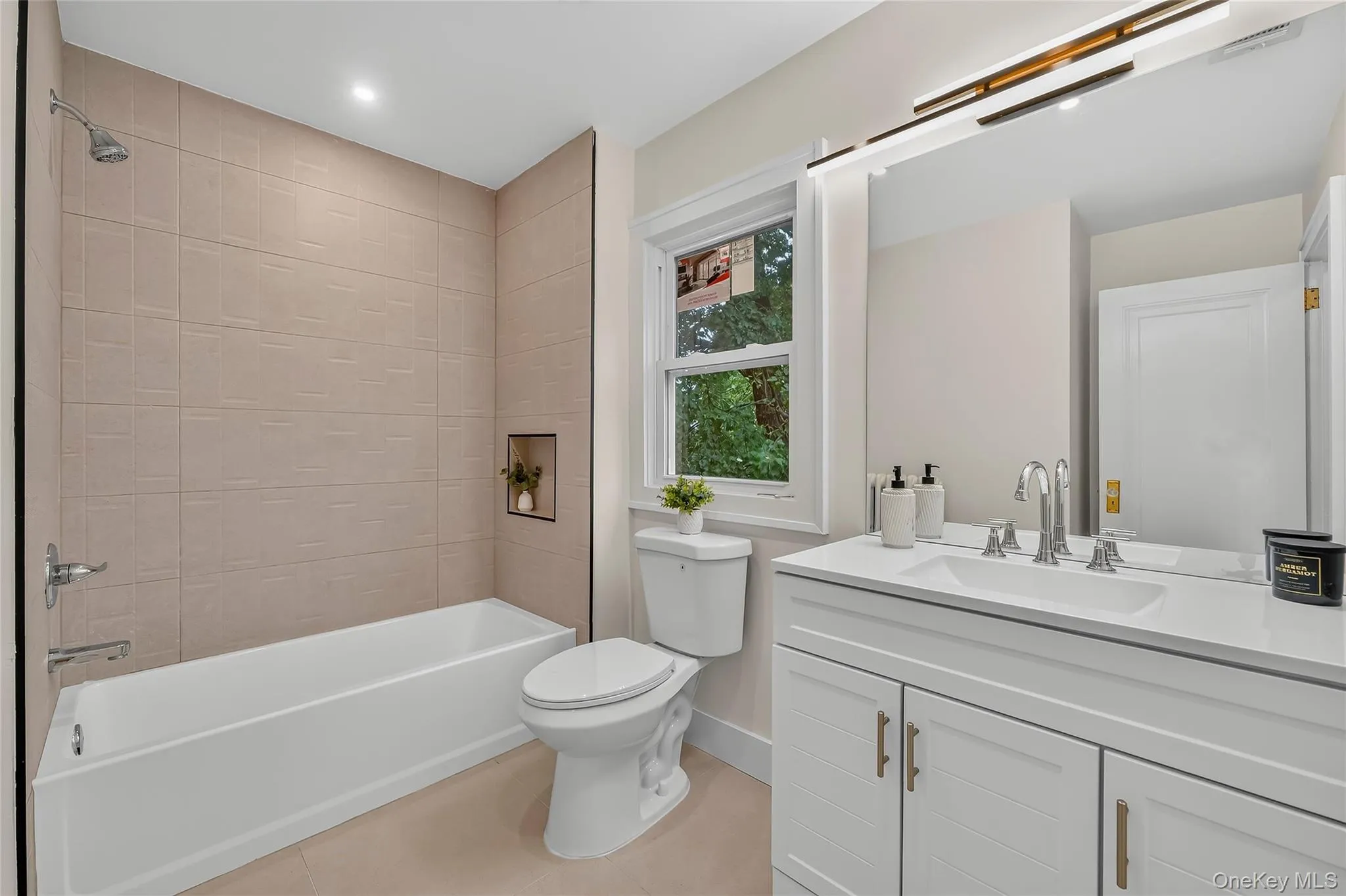Bathroom featuring a white vanity with a quartz countertop, a large mirror with integrated lighting, a tub/shower combination with tiled walls, and a recessed shower niche Bathroom featuring a white vanity with a quartz countertop, a large mirror with integrated lighting, a tub/shower combination with tiled walls, and a recessed shower niche