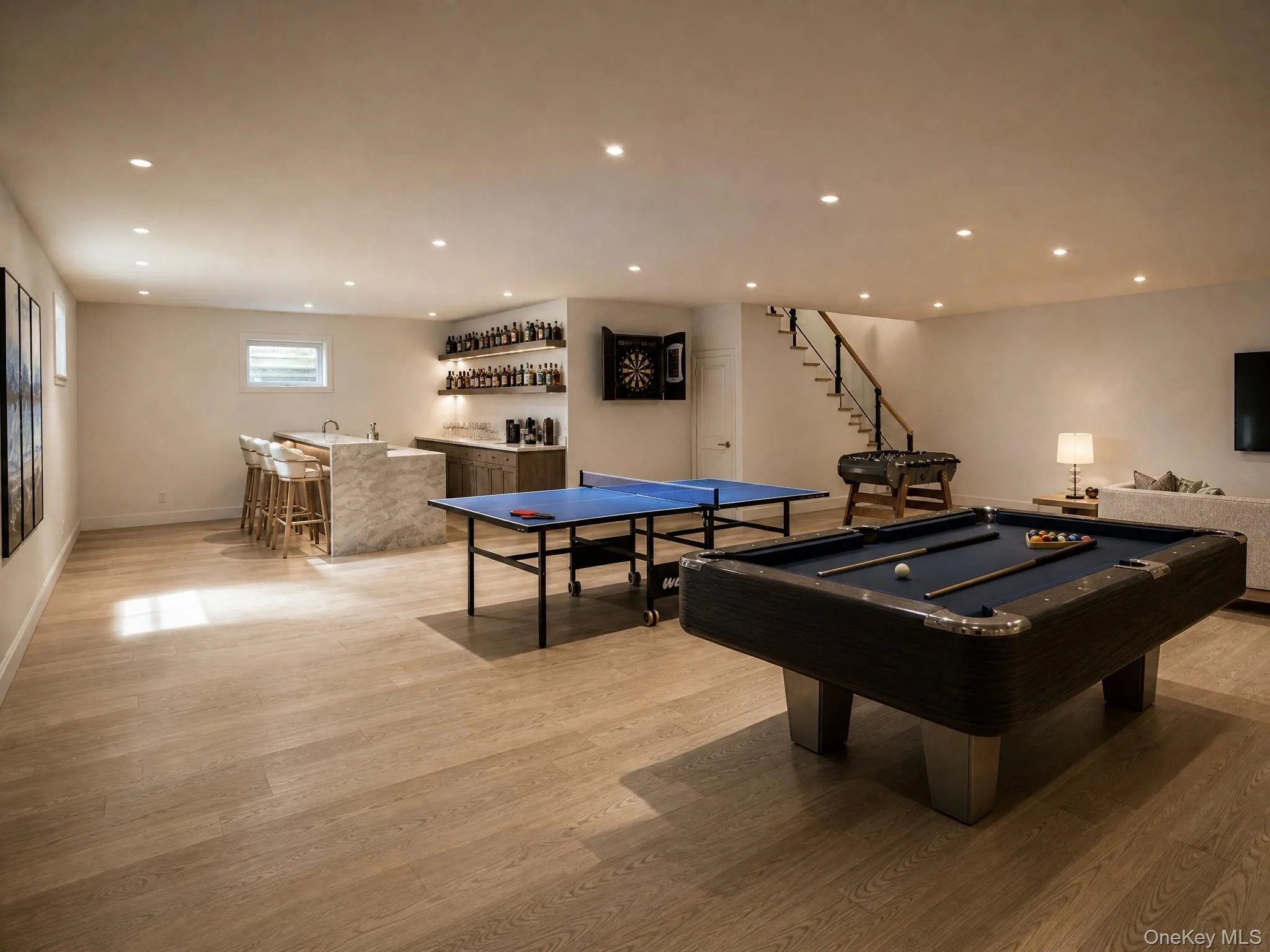 Expansive entertainment area featuring wood-finish flooring, a full wet bar with stone countertop, recessed lighting, and a staircase with glass panel railing Expansive entertainment area featuring wood-finish flooring, a full wet bar with stone countertop, recessed lighting, and a staircase with glass panel railing