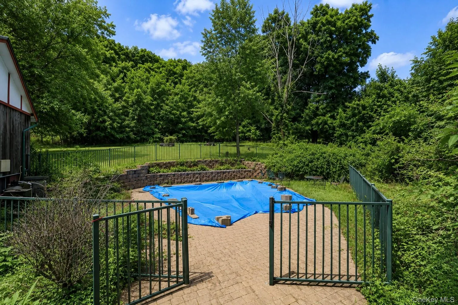 Fenced outdoor area featuring a swimming pool, paver patio, stone retaining wall, and mature trees surrounding the property- will be sold as is Fenced outdoor area featuring a swimming pool, paver patio, stone retaining wall, and mature trees surrounding the property- will be sold as is