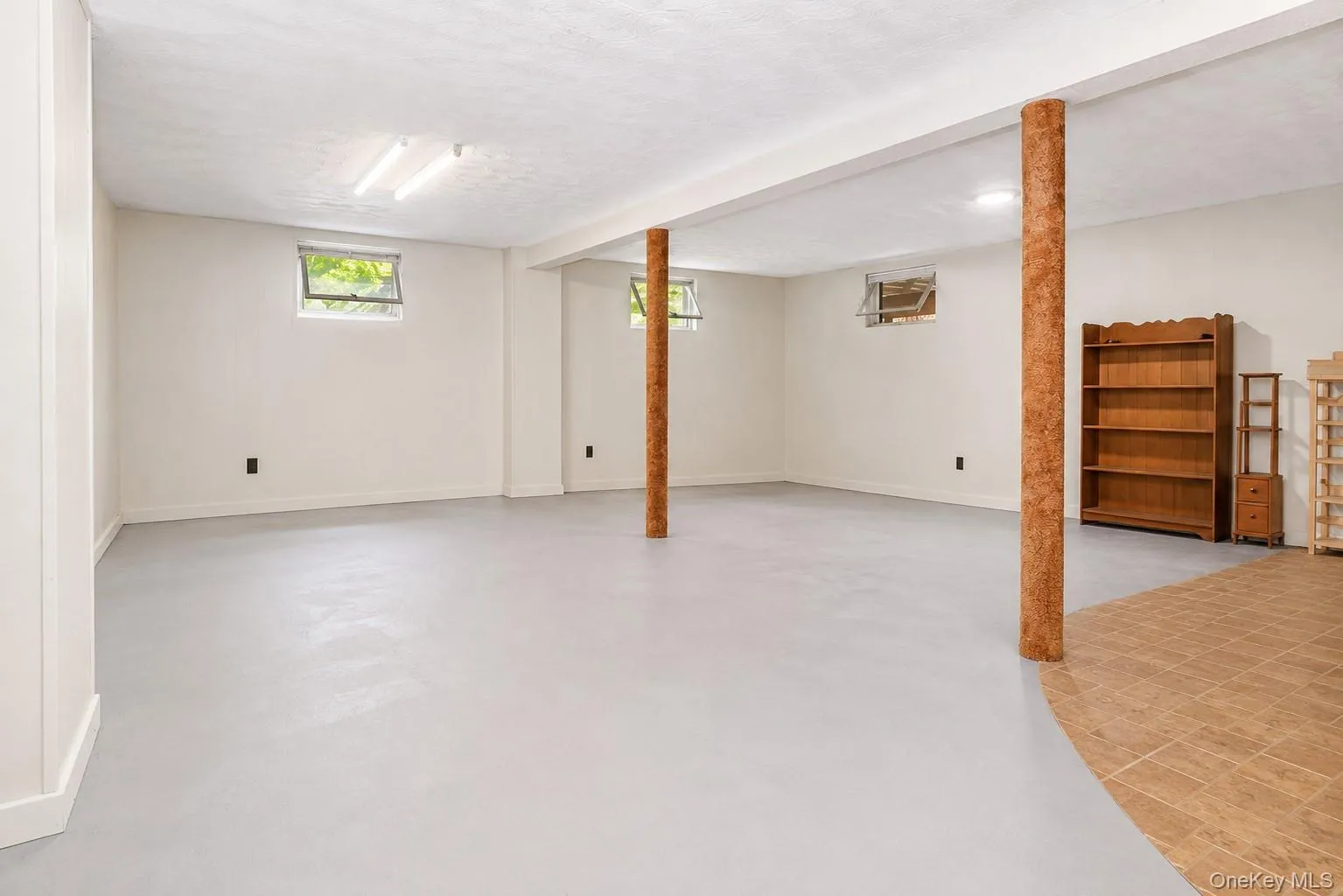 Spacious lower-level area featuring light gray flooring, white painted walls, and multiple windows for natural light Spacious lower-level area featuring light gray flooring, white painted walls, and multiple windows for natural light