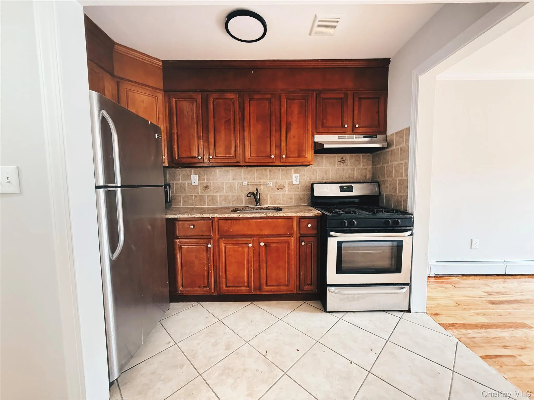 Kitchen featuring wood cabinetry, stainless steel appliances, tiled backsplash, and stone-look countertops. Kitchen featuring wood cabinetry, stainless steel appliances, tiled backsplash, and stone-look countertops.