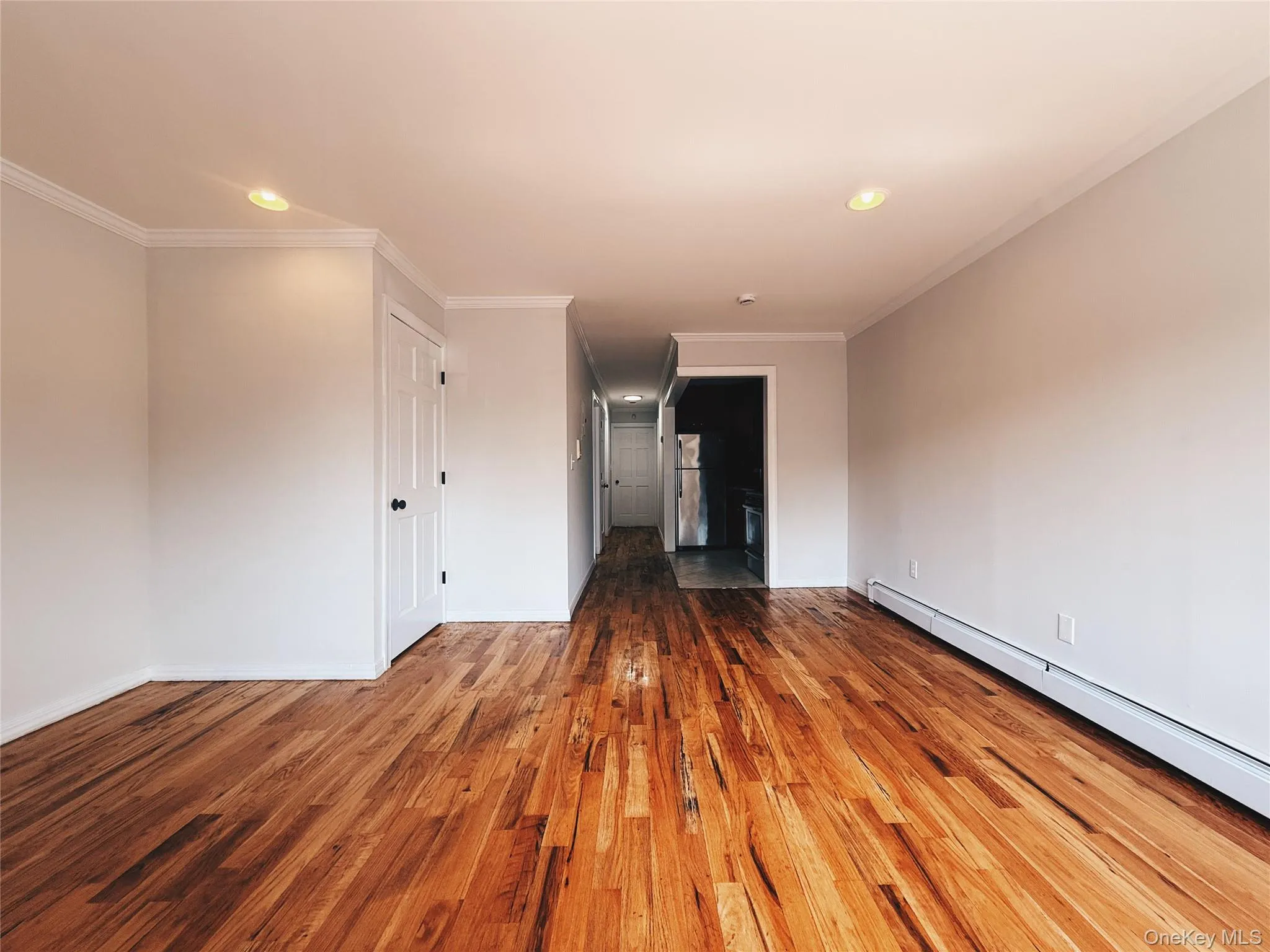 Spacious living area featuring wood-finish flooring, ample natural light from a large window, recessed lighting, and crown molding. Spacious living area featuring wood-finish flooring, ample natural light from a large window, recessed lighting, and crown molding.